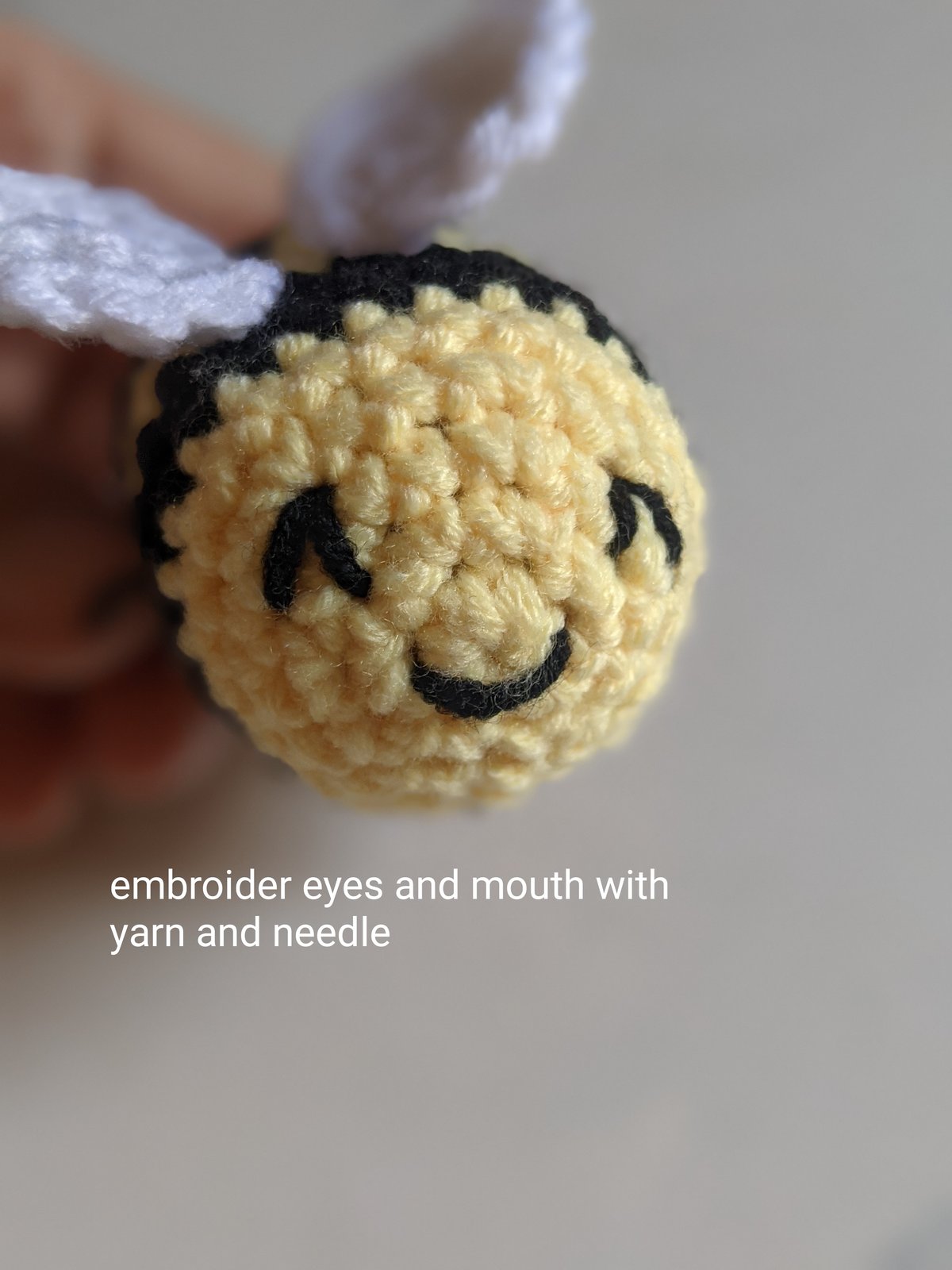 Close-up of the finished bumble bee amigurumi face with two black embroidered eyes and a curved smiling mouth on the yellow front of the body