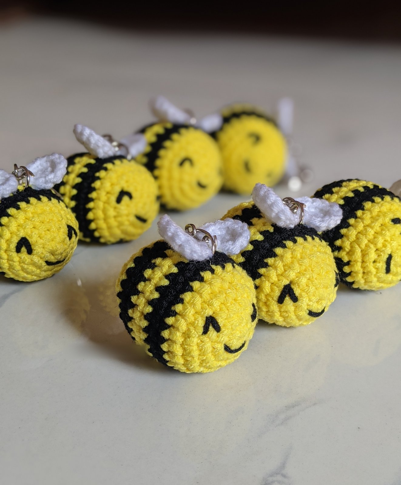 Group of seven yellow and black crocheted bumble bee amigurumi with white wings on a marble surface, top-down view