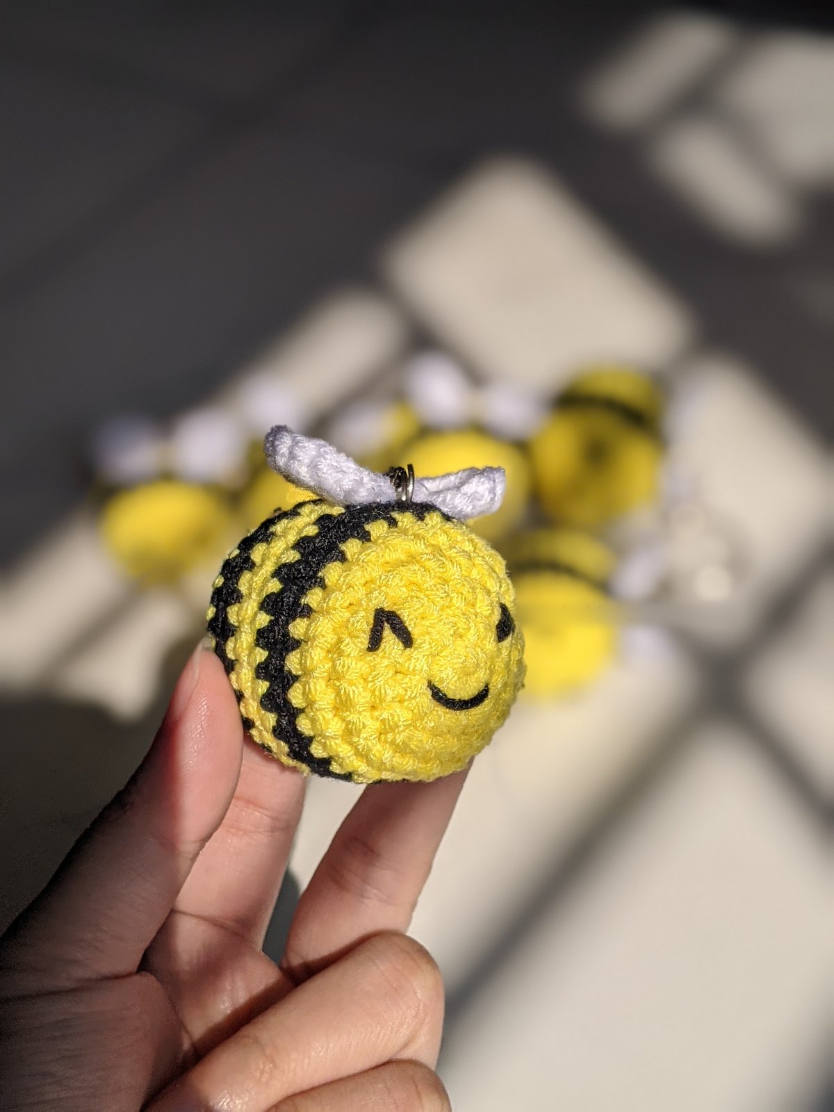 Single crocheted bumble bee amigurumi with yellow body, black stripes, white wings and embroidered smiling face held in a hand