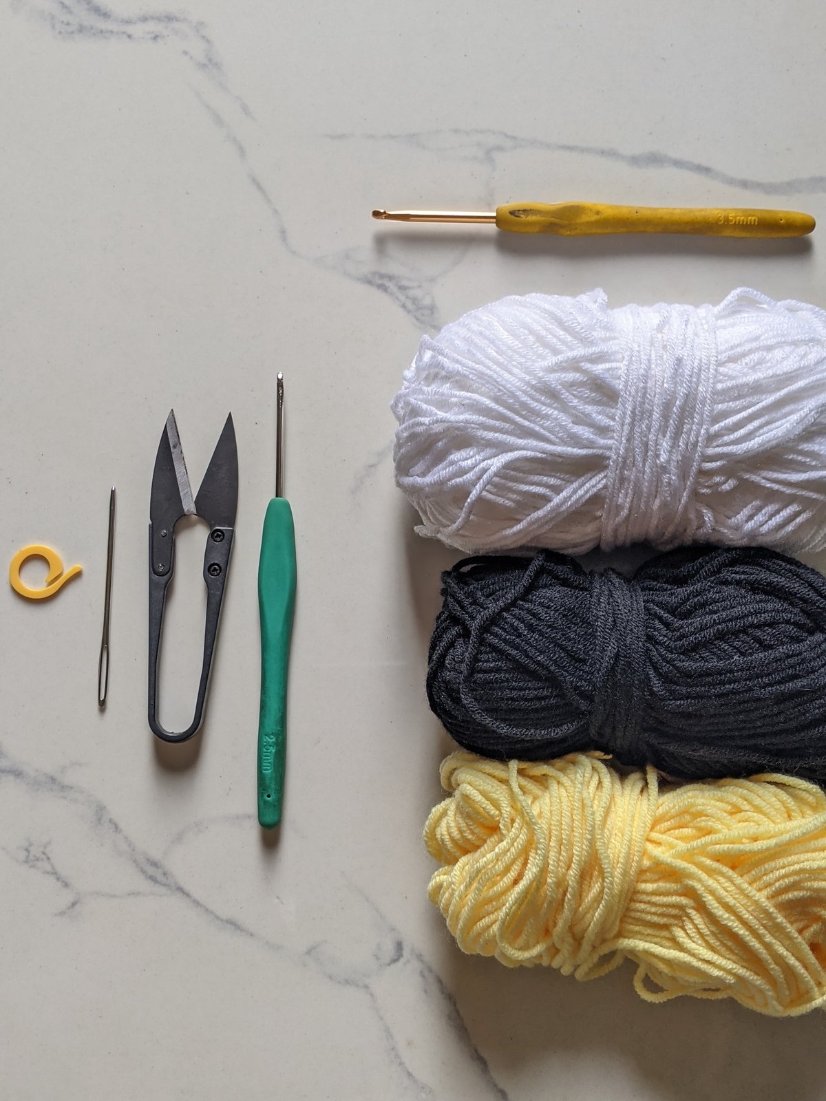 Materials flat lay for the bumble bee crochet pattern: yellow, black and white milk cotton yarn, a 3.5 mm crochet hook, scissors, tapestry needle and stitch marker