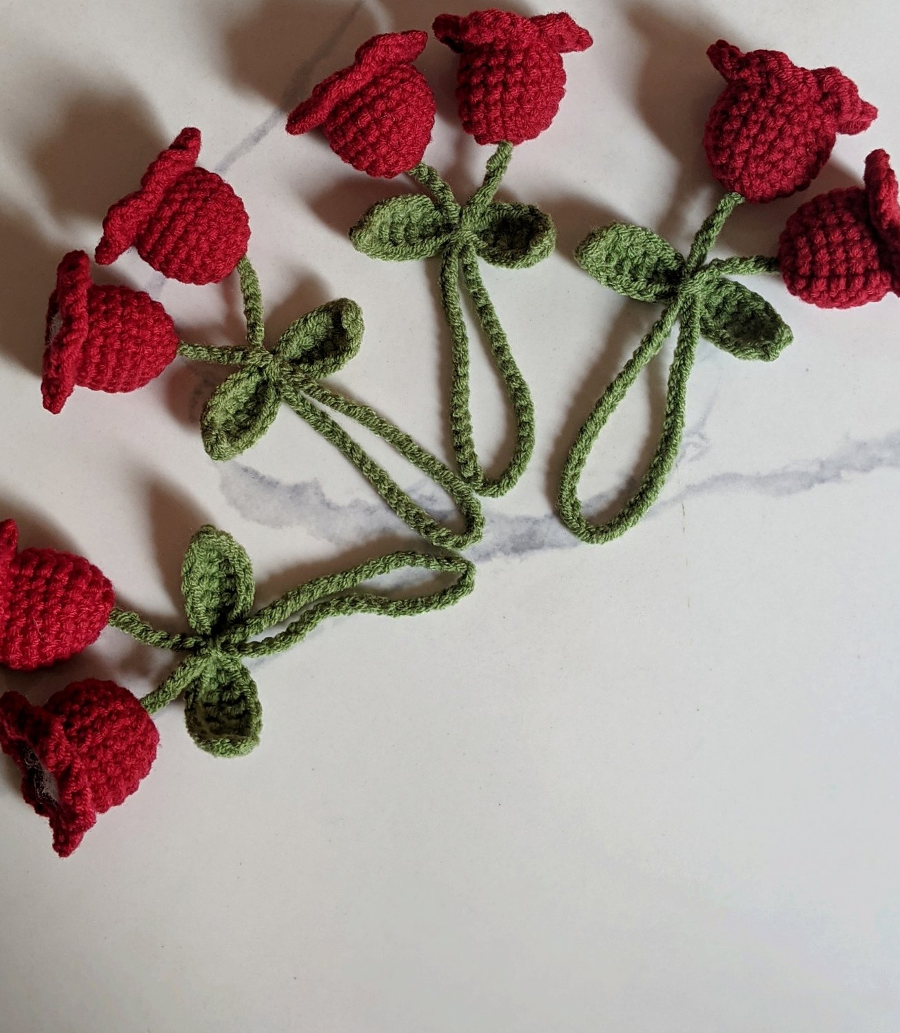 Four finished lily of the valley crochet bag charms in red and green arranged on white marble, top-down view