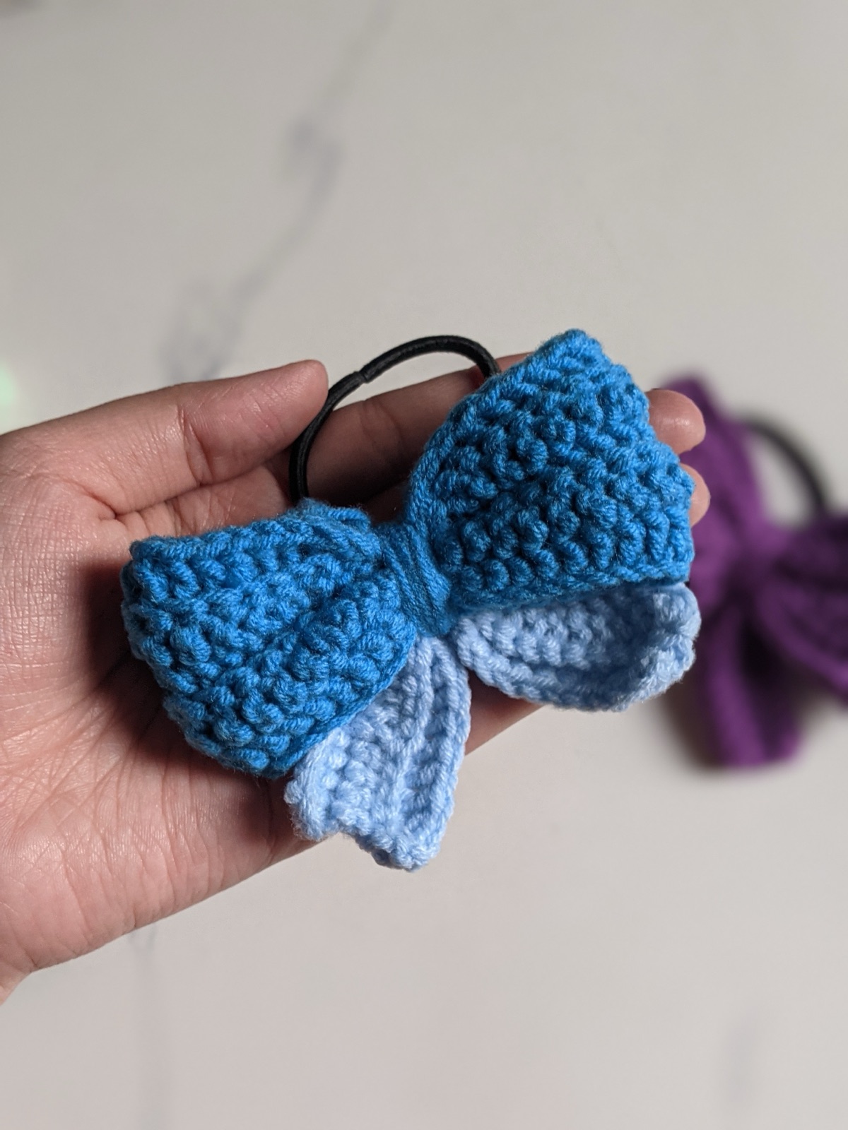 Crocheted blue and light blue puffy bow hair tie held in an open hand to show palm-size scale