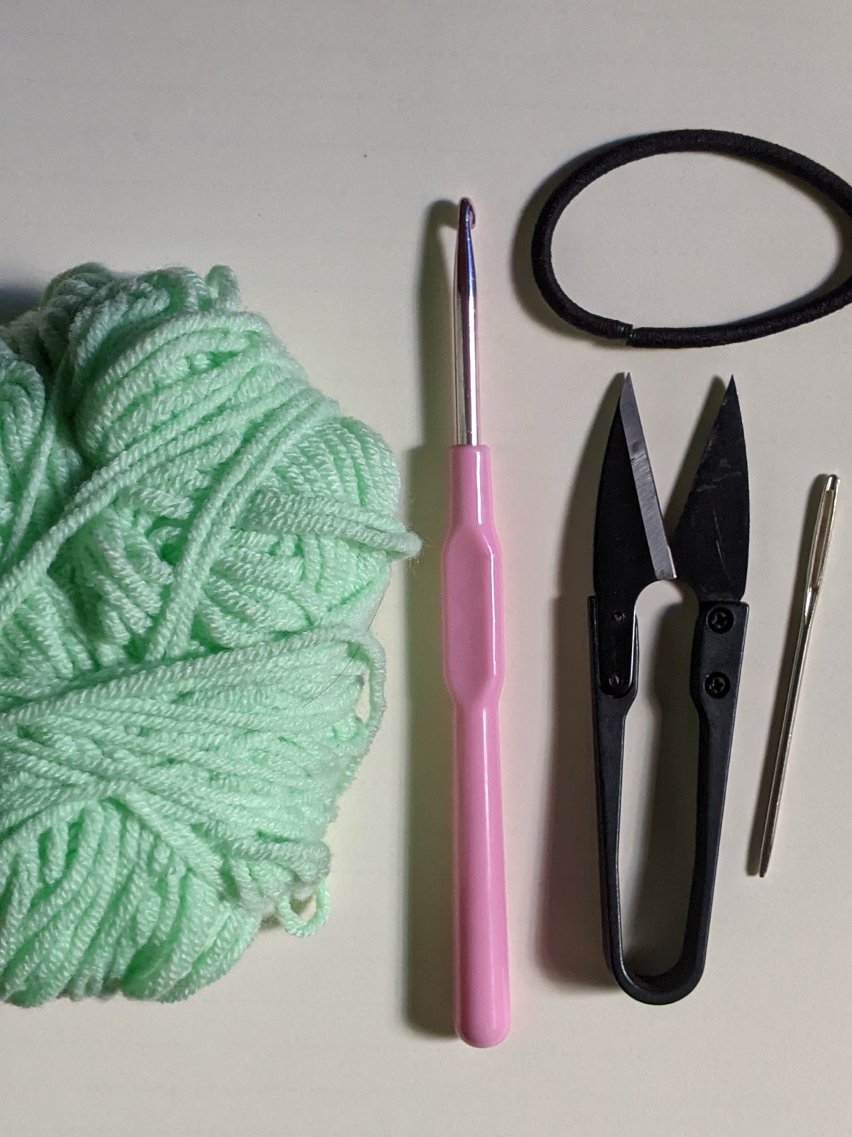 Flat lay of crochet supplies: a ball of mint cotton yarn, a 3 mm hook, scissors, and a tapestry needle