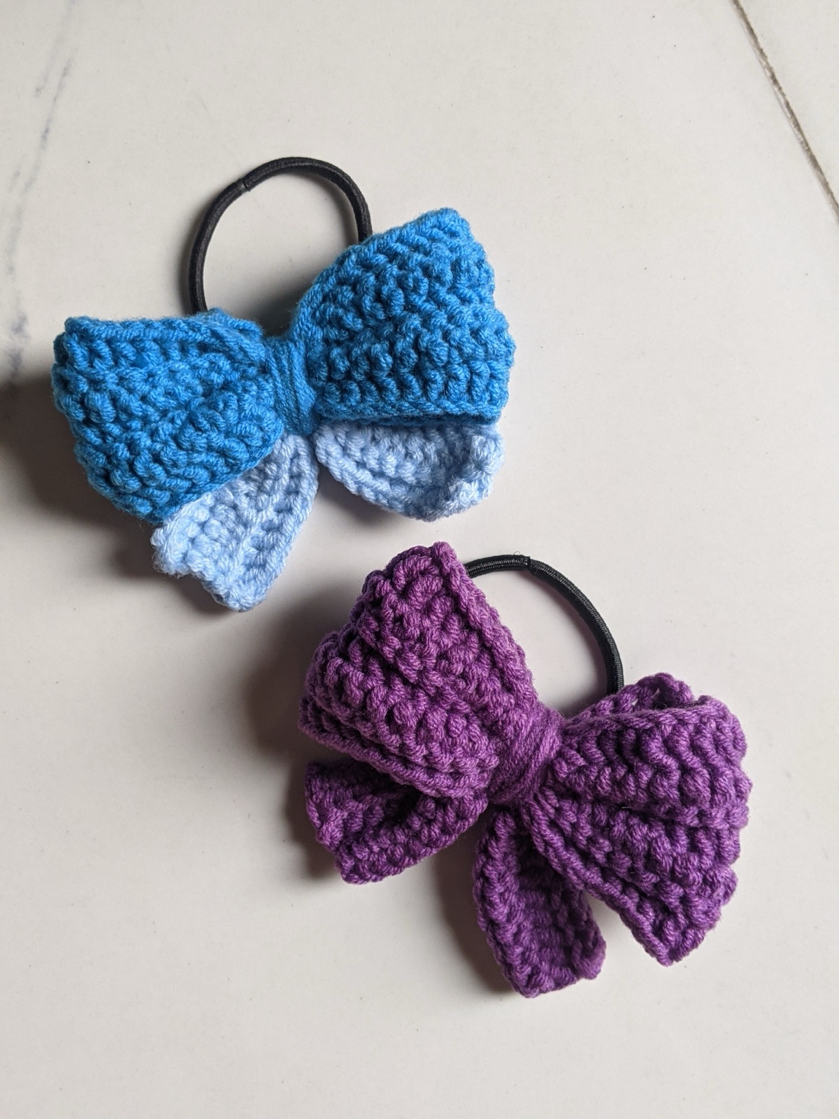Two puffy crochet bows side by side in blue and purple, showing different colorways for a keychain