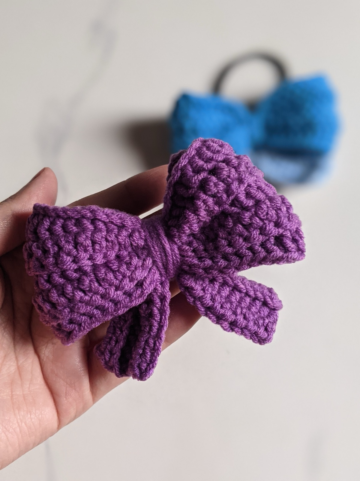 A crocheted purple mini bow held in an open hand to show its palm-size scale