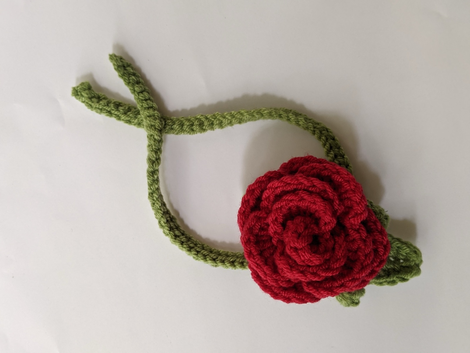 Single red and green crochet rose gajra laid flat with long green tie strings fanned out on a white background