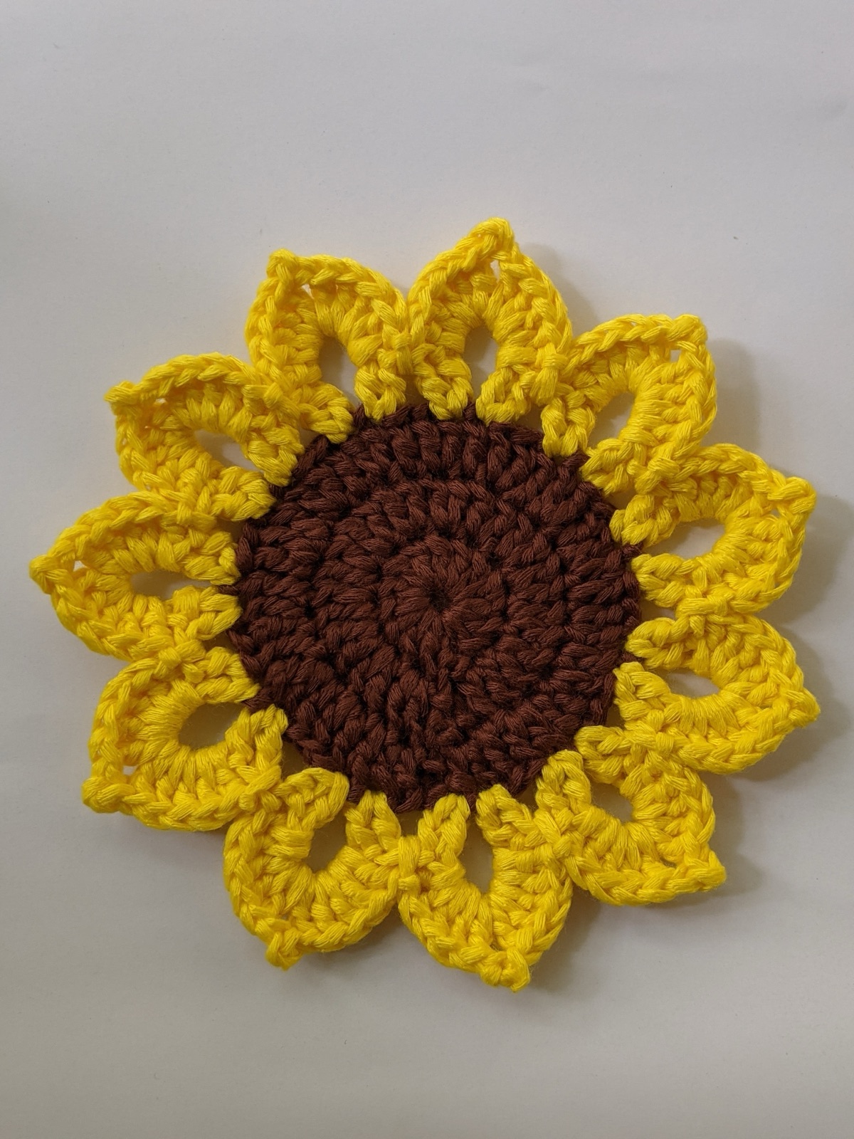Top-down photo of a finished crocheted sunflower coaster with a dark brown center and 11 yellow petals on a white background