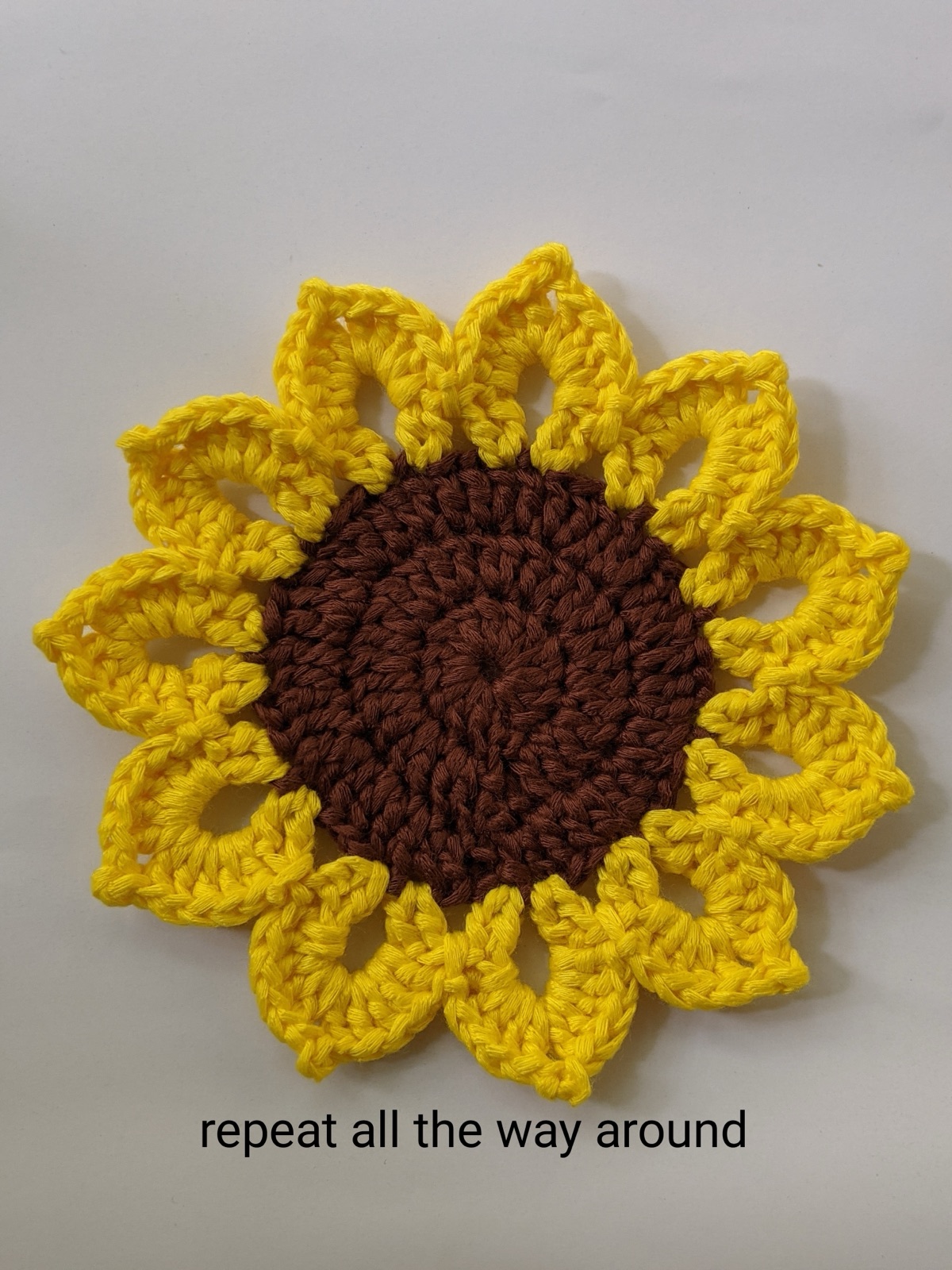 Top-down view of a completed sunflower coaster after repeating the round-5 petal pattern all the way around, finished with 11 yellow petals around a brown center