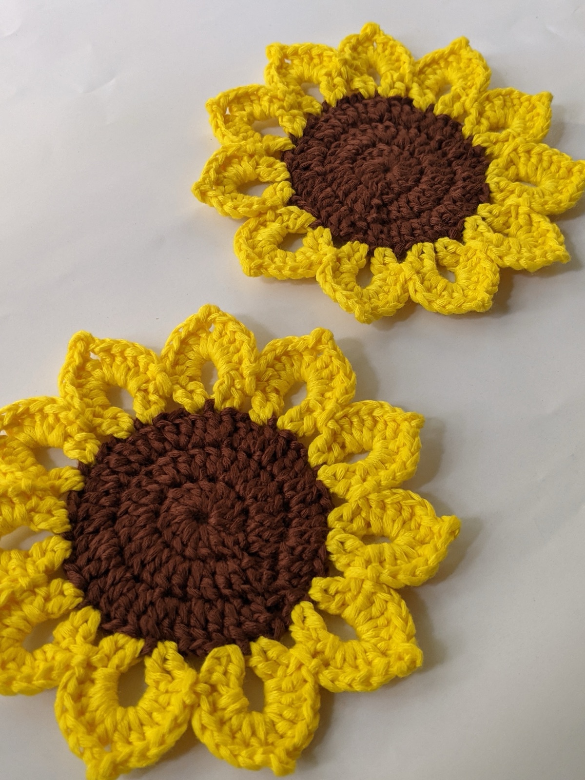 Pair of crocheted sunflower coasters with brown centers and yellow petals arranged at an angle on a white surface