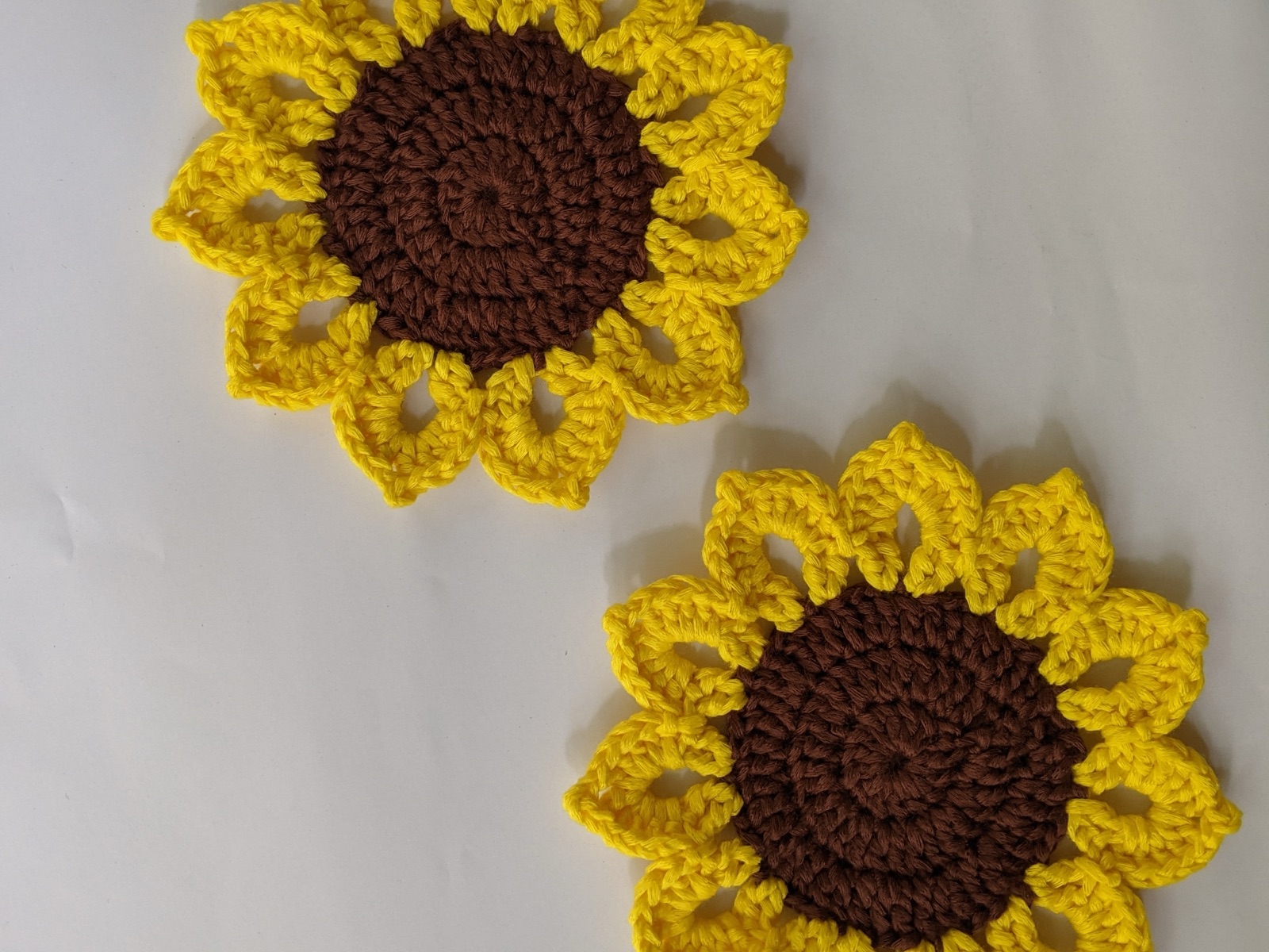 Pair of finished sunflower coasters laid flat on a white surface with their petals slightly overlapping