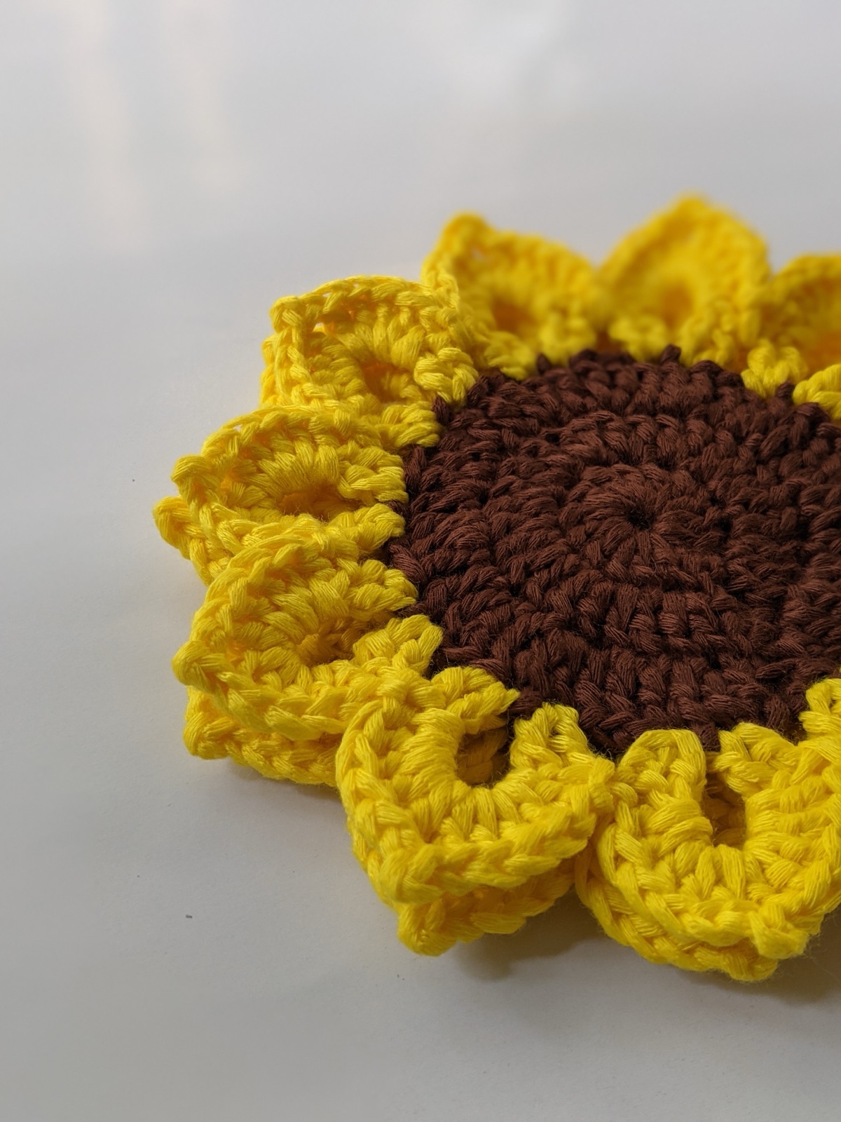 Close-up macro photo of a finished sunflower coaster showing the texture of the yellow petal stitches and the firm brown center