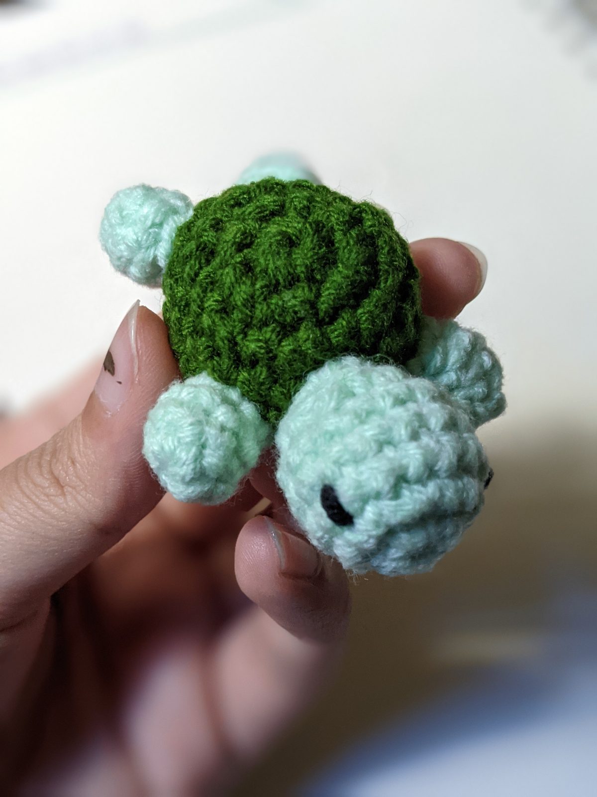 Tiny crocheted turtle held in a pinch grip from above