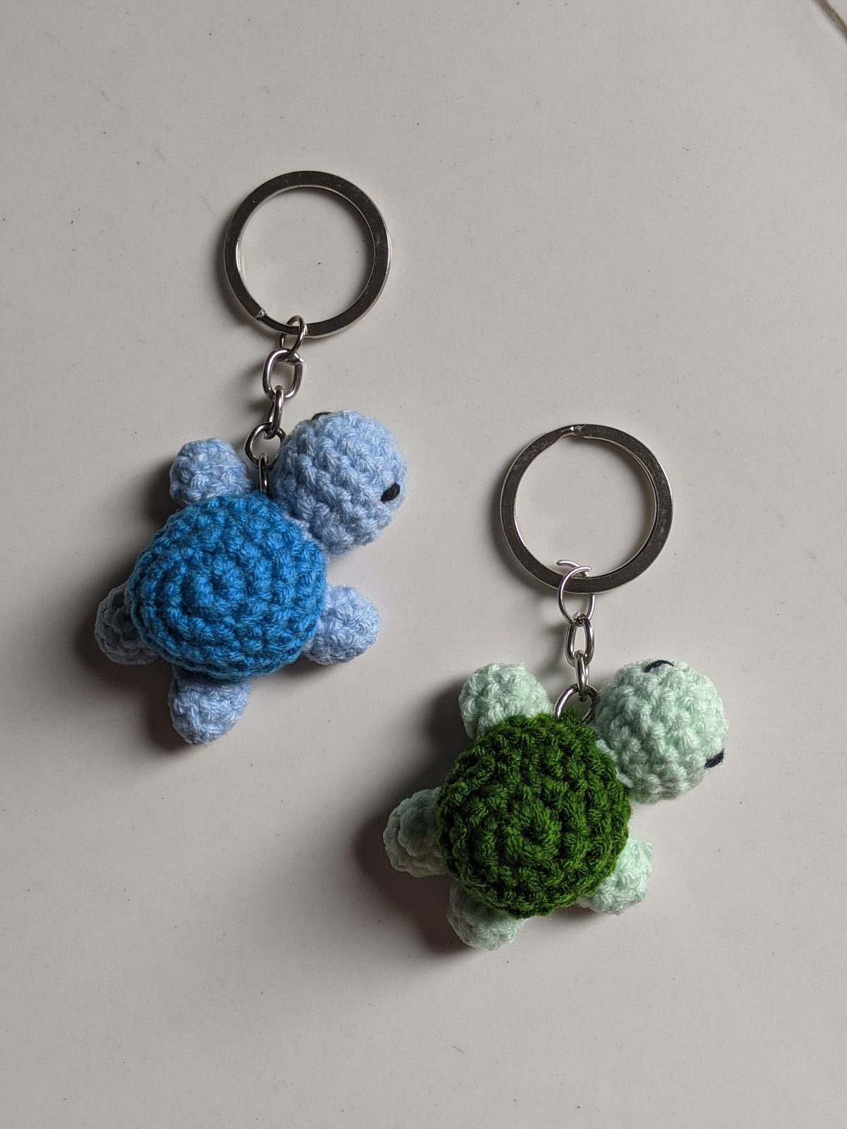 Close-up of two tiny crocheted turtle keychains showing the silver split rings prominently attached to the top of each shell
