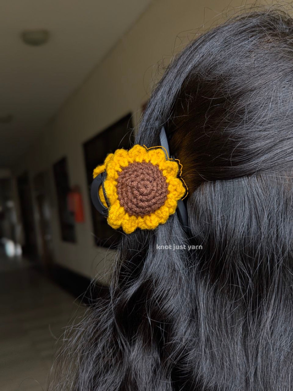 Crocheted yellow sunflower with a brown center clipped into long dark wavy hair, worn at the side of the head