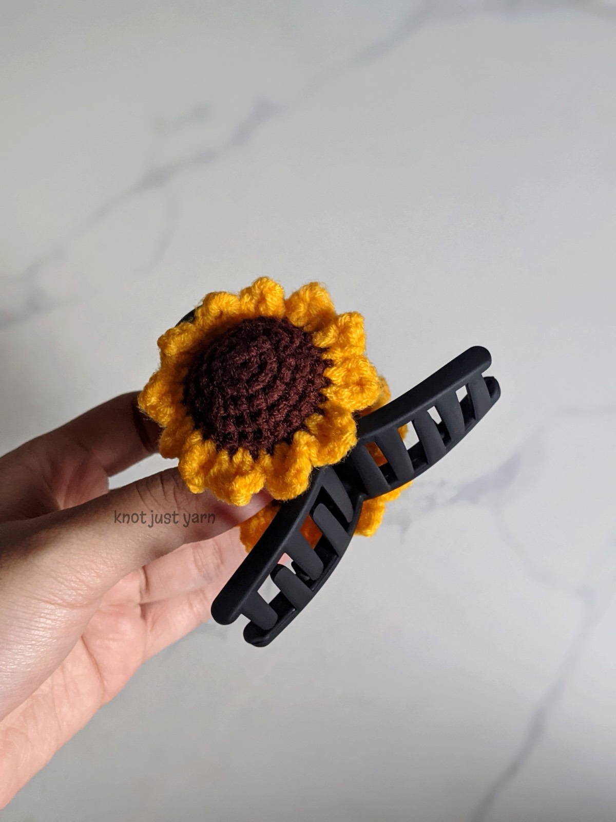 Hand holding a single sunflower clip attached to a large black claw clip, showing the real size of the finished piece