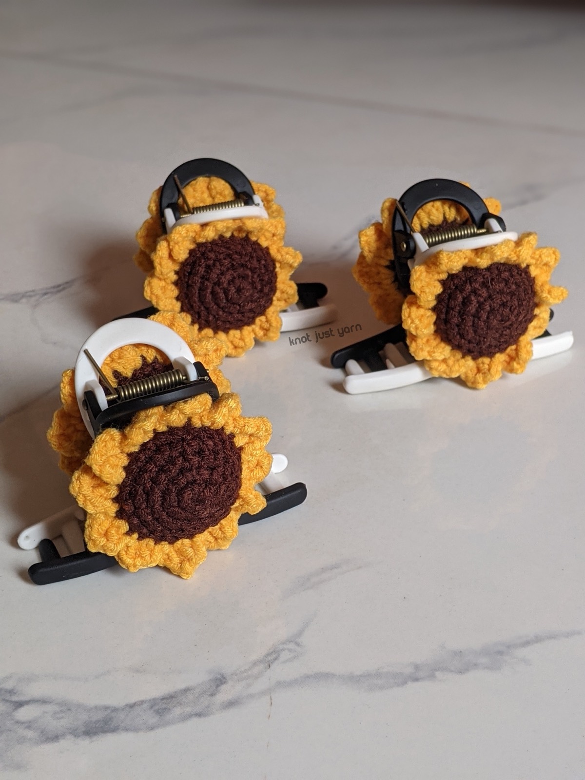 Three finished sunflower claw clips on a white marble surface, two upright and one face up showing the petal detail