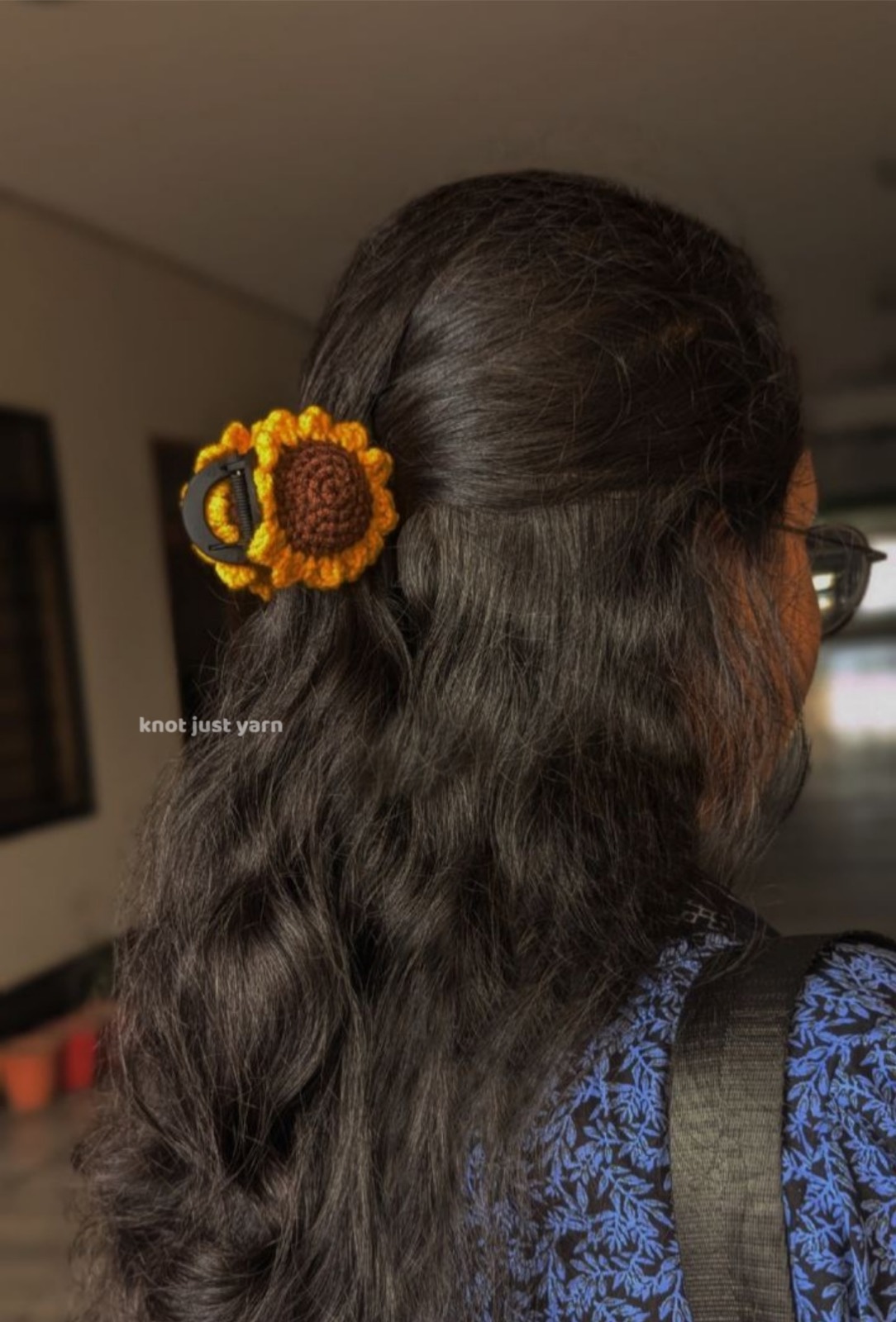 Crochet sunflower claw clip worn from behind in long dark hair, holding a half-up section