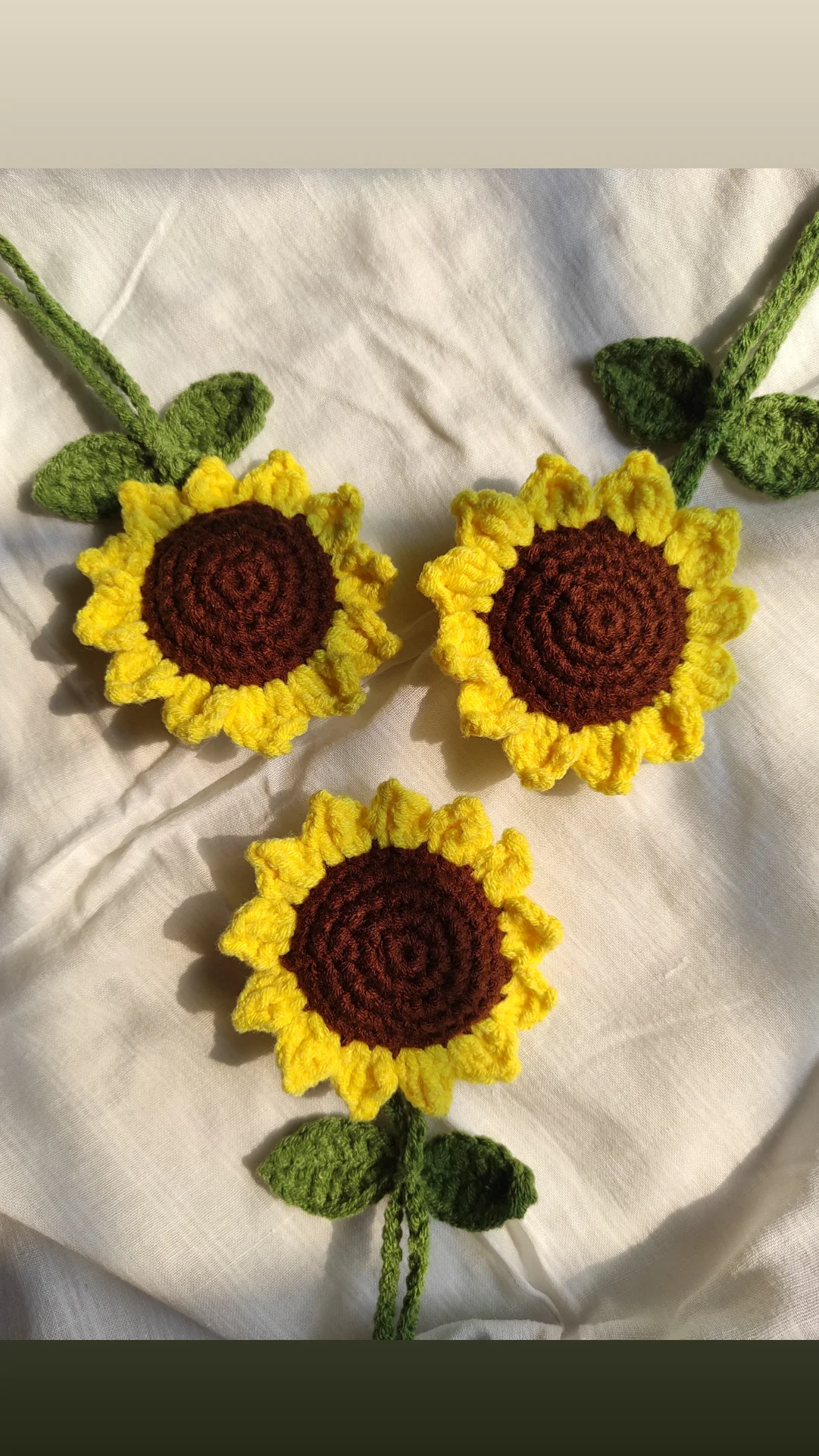 Three crochet sunflowers with green leaves and stems grouped into a small bouquet on white fabric