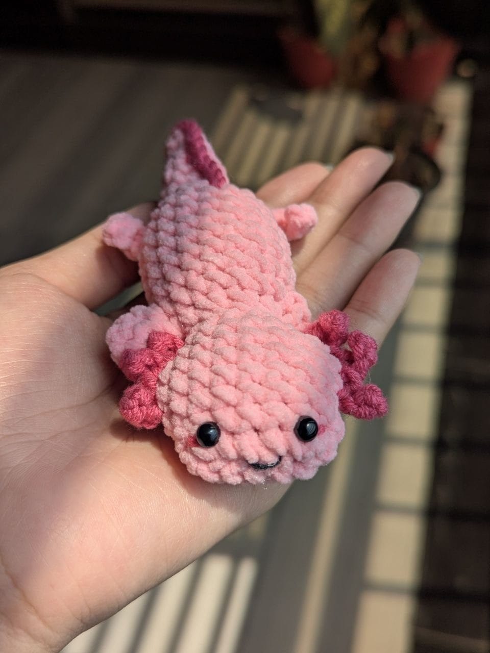 Completed mini pink crochet axolotl amigurumi resting on an open palm in warm light