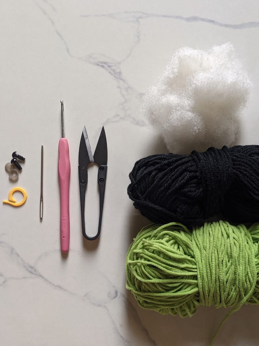 Materials for the crochet leggy frog: green plush yarn, black yarn, 3mm hook, scissors, safety eyes, stitch marker and fiberfill