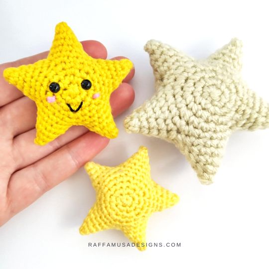Three crocheted three-dimensional stars in yellow and cream, one with an embroidered smiling face held in a hand for scale