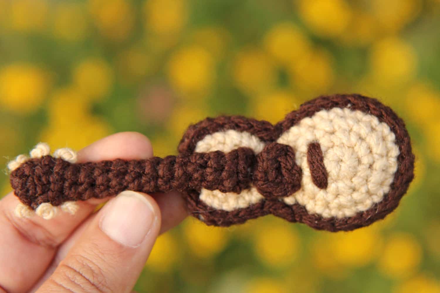 A small brown and cream crochet acoustic guitar keychain, by Chai Coffee Crochet