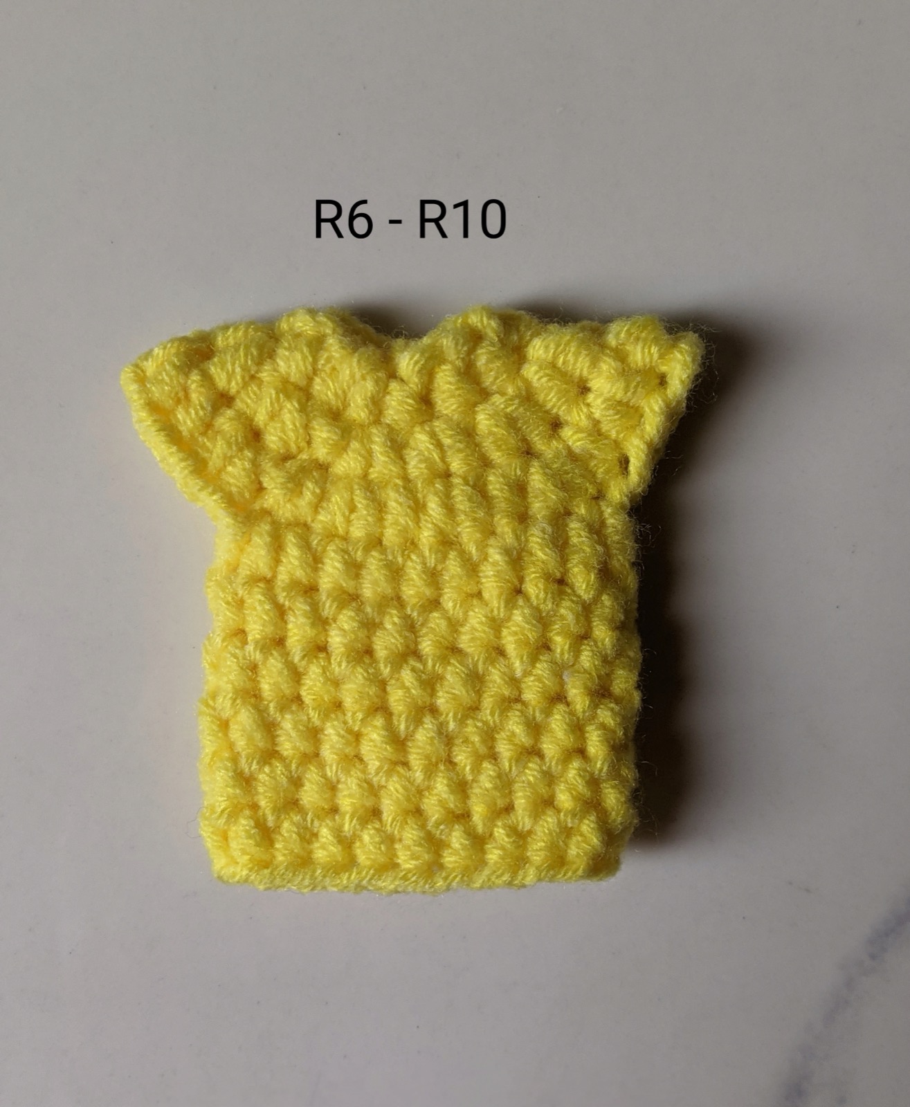 The finished flat yellow jersey body with the two skipped-stitch armholes forming small points at the shoulders