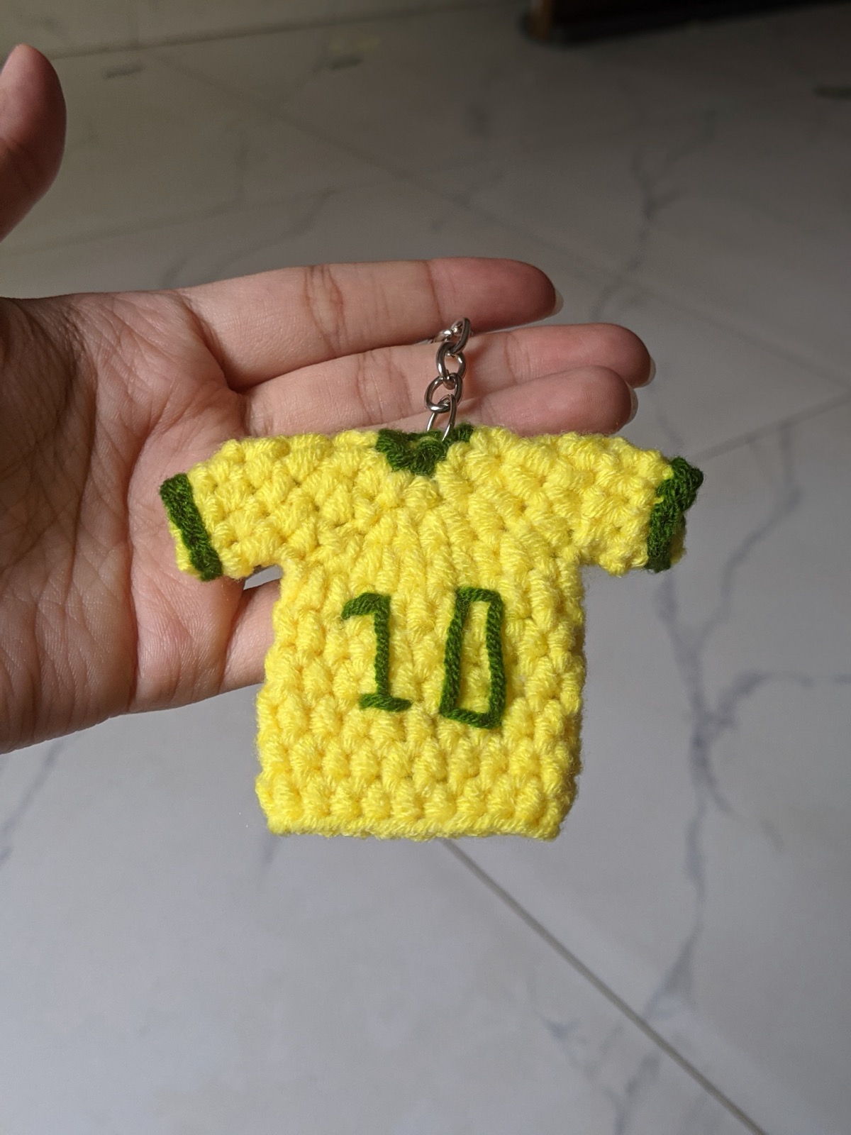 A mini crochet football jersey keychain held in a hand, showing the sleeves and the number on the back