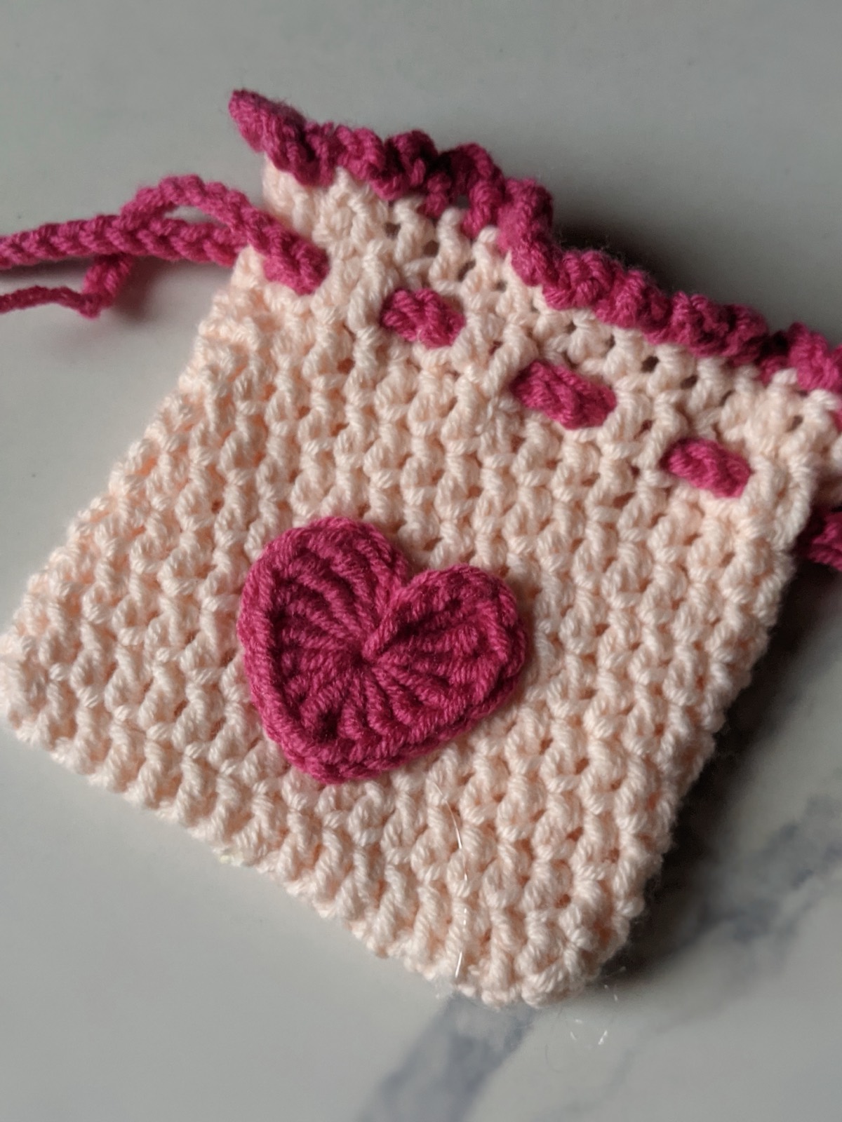 Close up of the finished crochet pouch showing the dark pink picot border, the woven drawstring holes and the heart on the front