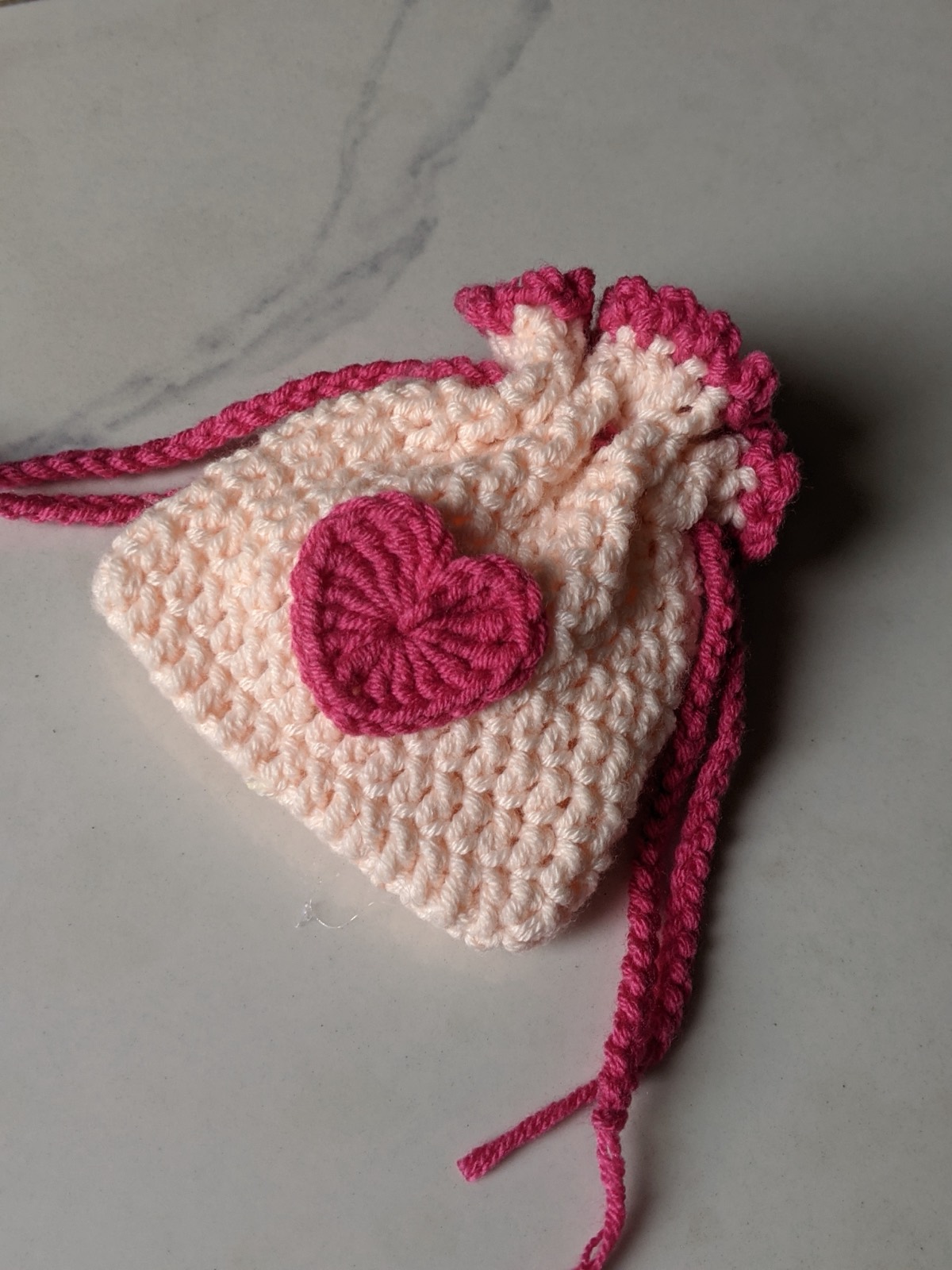 The finished crochet mini pouch cinched shut on a marble surface with both drawstrings pulled