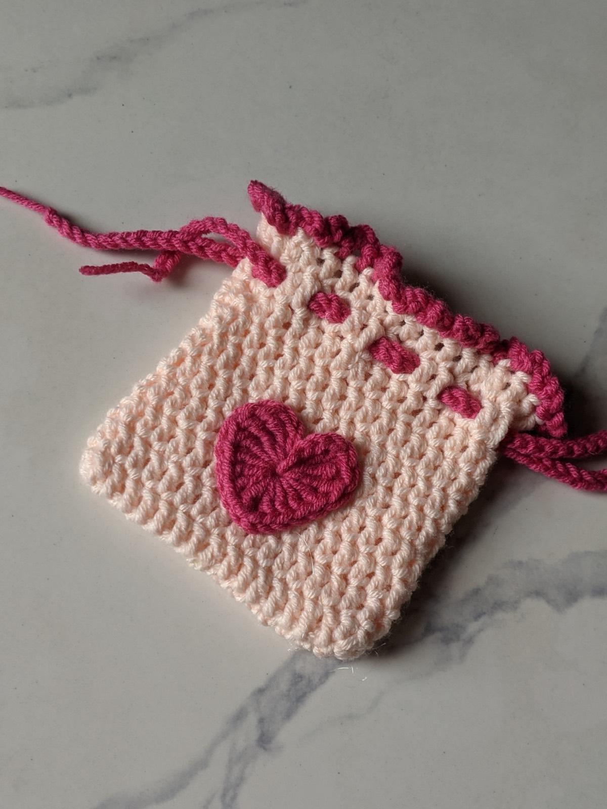 The finished crochet mini pouch lying flat and open with the drawstrings loose, showing the square shape and the heart on the front