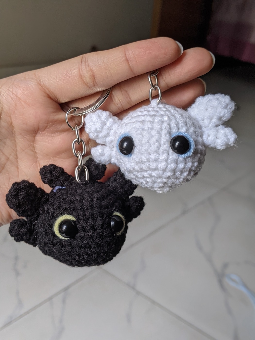 The black and white crochet dragon keychains hanging from silver chains and split rings, held up in a hand