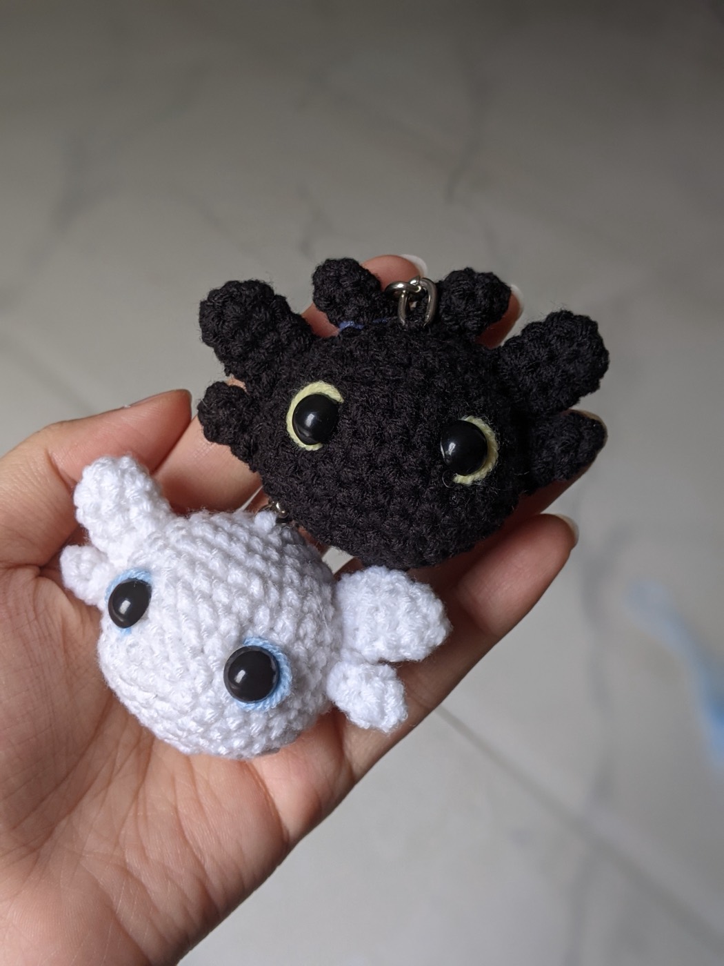 A black crochet dragon and a white crochet dragon resting side by side in an open palm