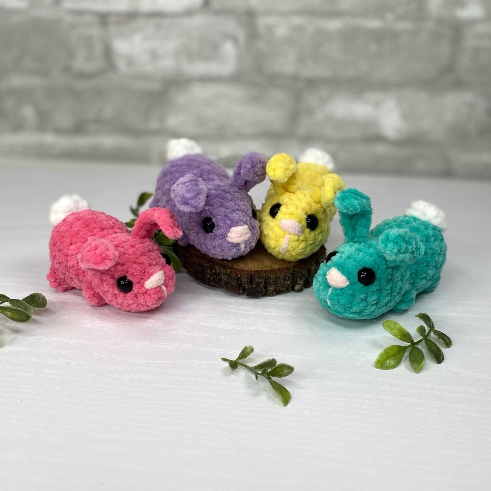 Four no-sew crochet jelly bean bunnies in pink, purple, yellow and turquoise chenille yarn with white pom pom tails, from Darling Maple Designs