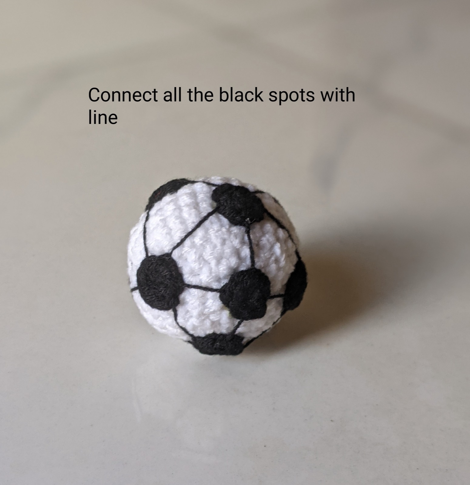 The finished crochet soccer ball with thin black embroidered lines joining all ten black spots
