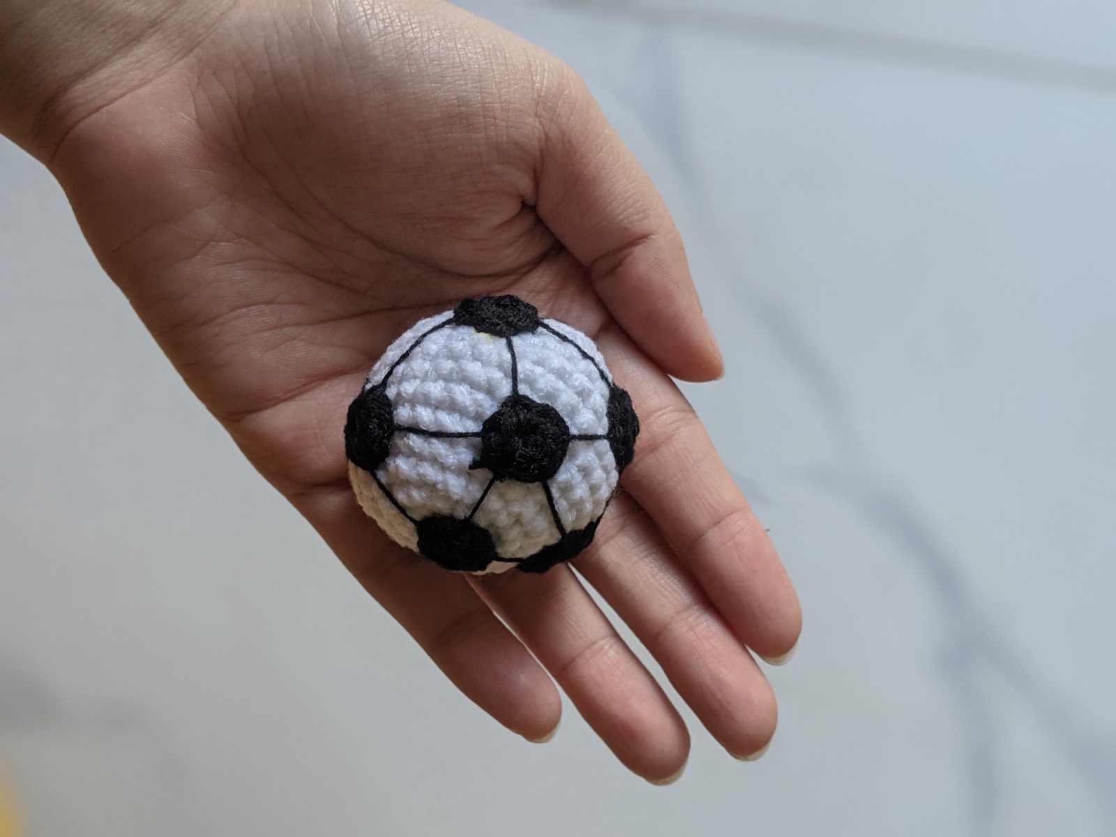 A small white and black crochet soccer ball resting in an open palm, about two inches across
