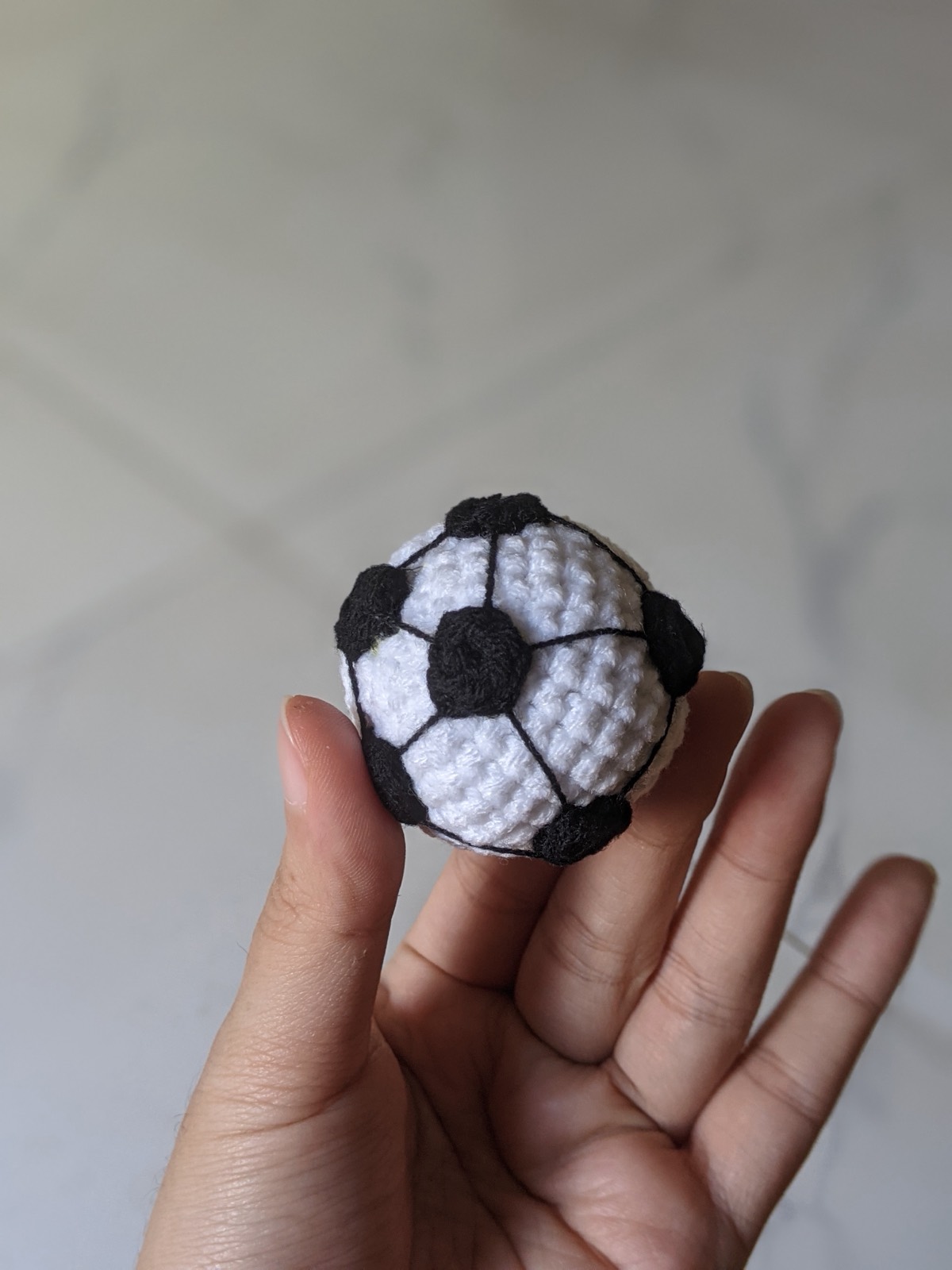 The finished crochet soccer ball keychain held between finger and thumb, showing the black spots and embroidered lines from the side