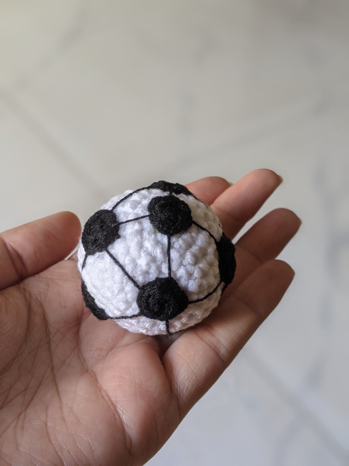 The crochet soccer ball keychain resting on an open palm showing its scale against the fingers