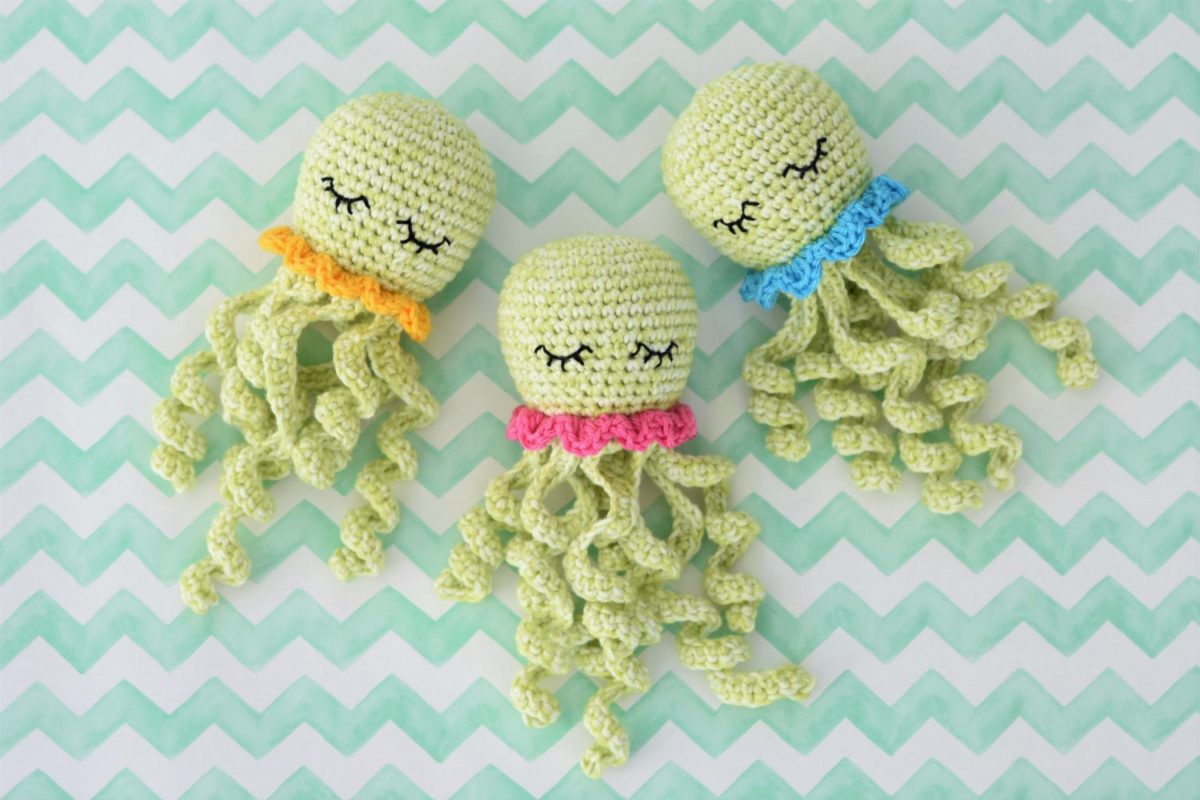 Three pale green crochet octopuses with sleepy embroidered eyes and coloured ruffle collars on a mint chevron background