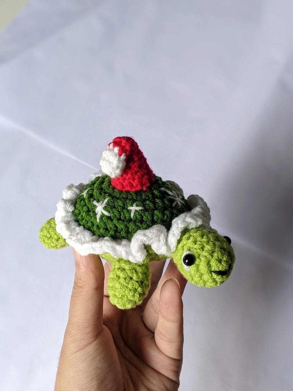 Finished crochet Christmas tortoise seen from the front, with safety eyes, a small smile and a bent red Santa hat