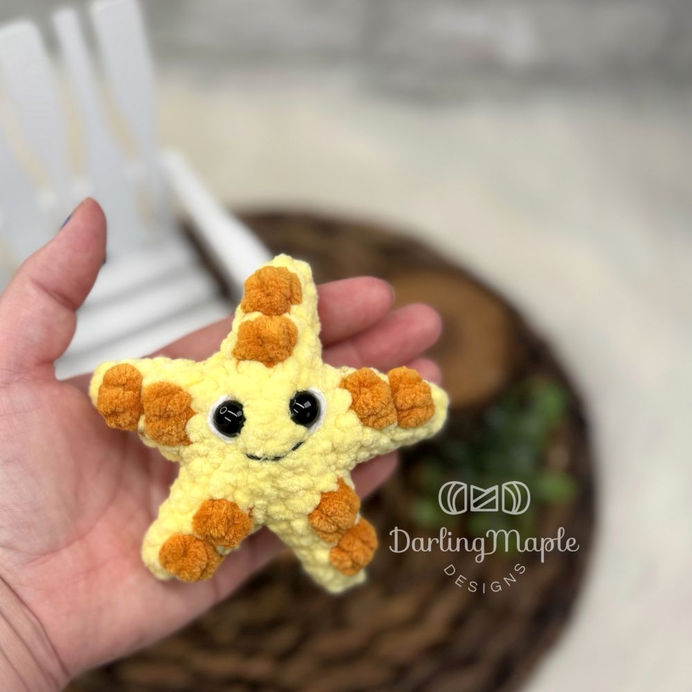 Yellow and orange plush crochet starfish with safety eyes and a smile held in a hand