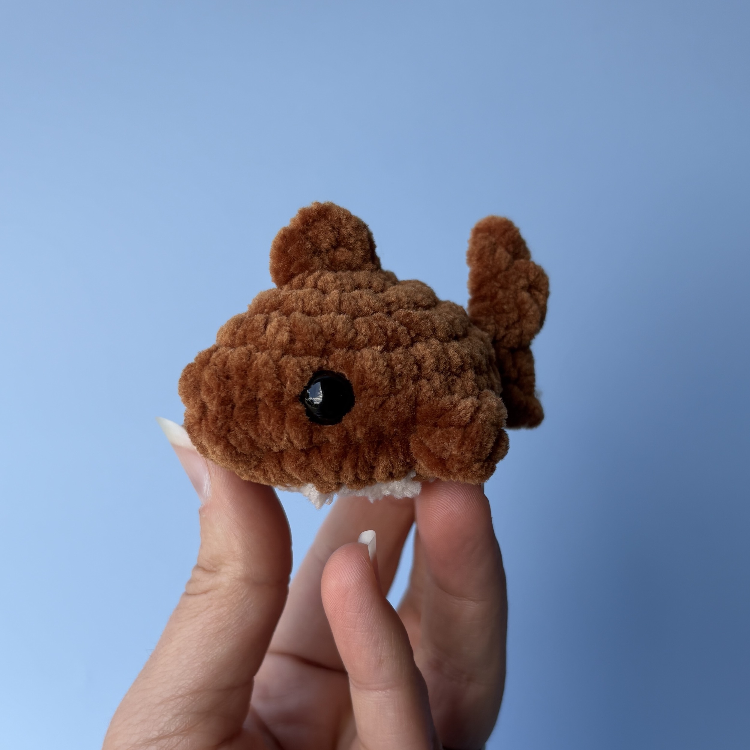 Small brown chenille crochet shark held between two fingers against a blue background