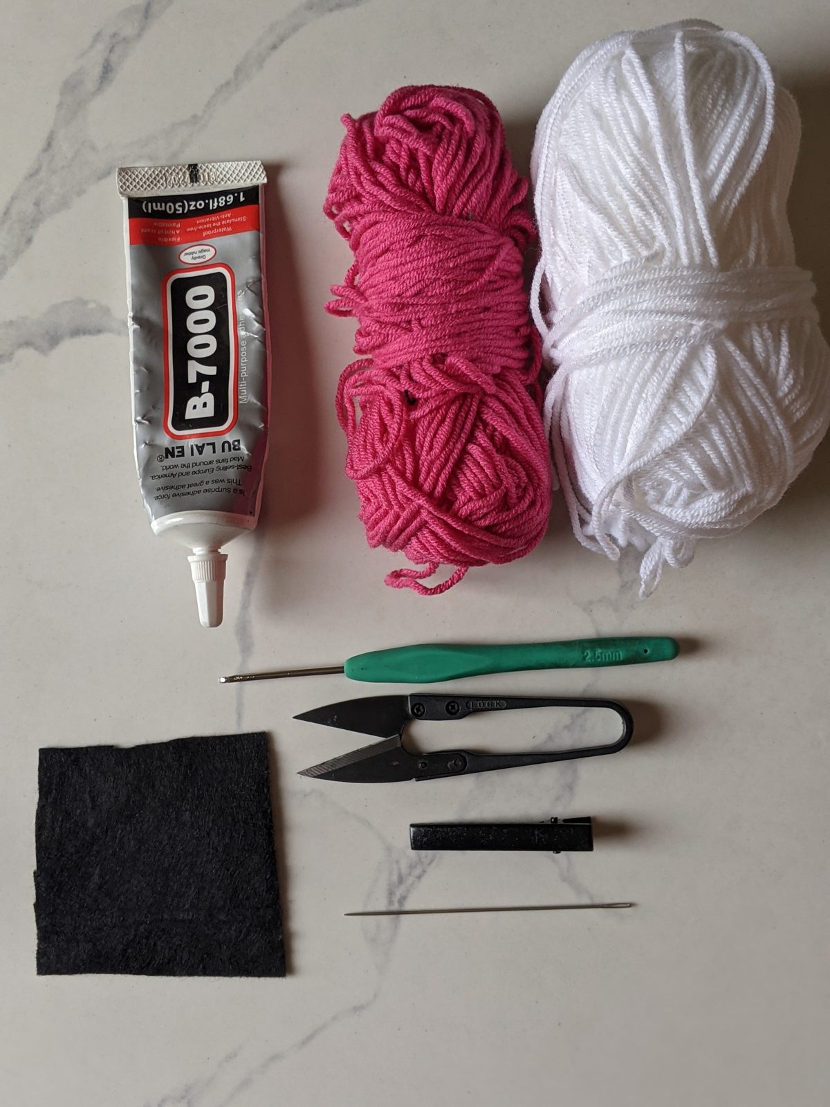 Materials for the crochet daisy hair clip: B-7000 glue, pink and white milk cotton yarn, a 2.5 mm crochet hook, thread snips, black felt, an alligator clip and a yarn needle