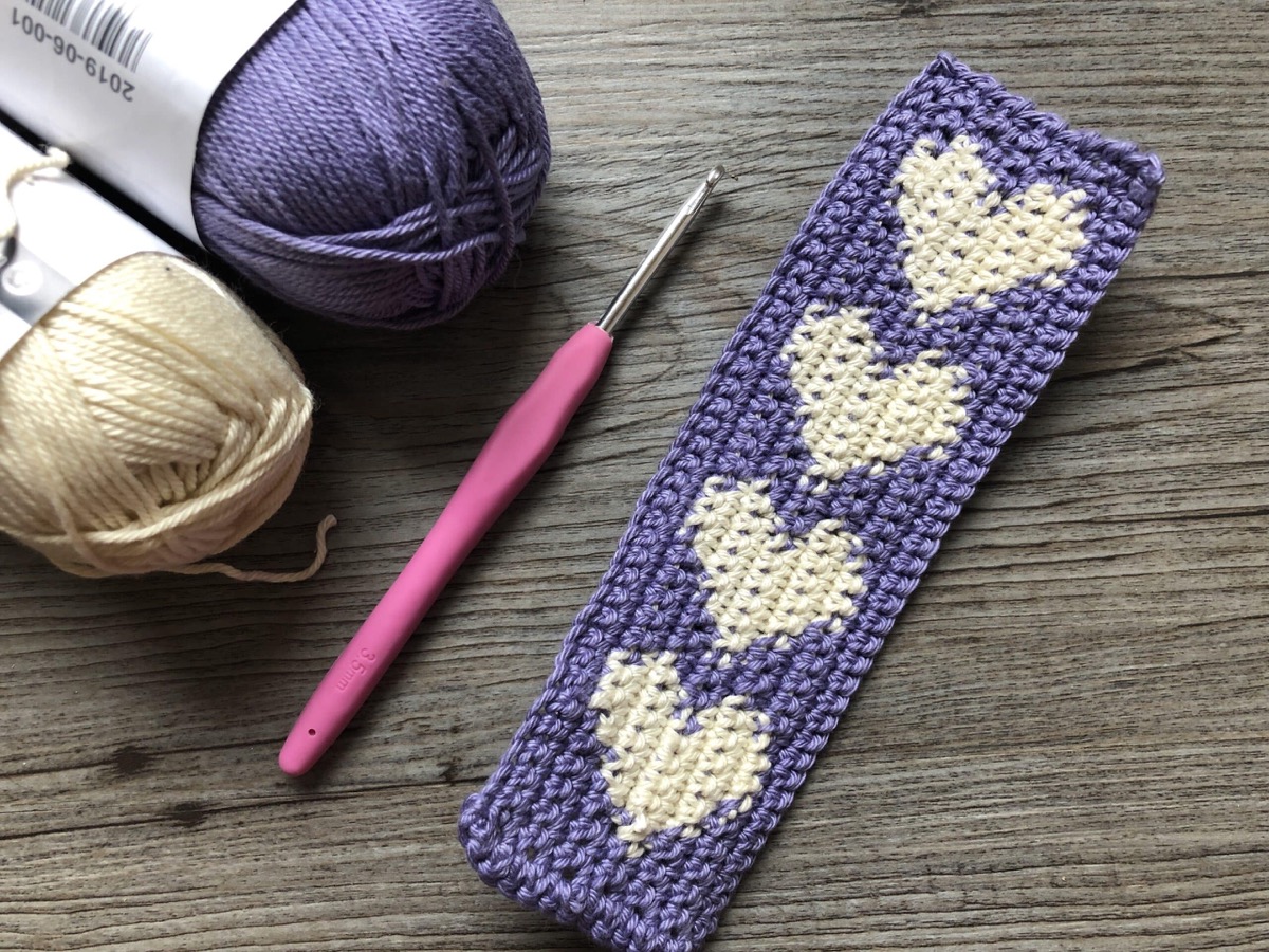 A slim crochet bookmark made of small linked hearts with a tassel at the end, designed by Rich Textures Crochet