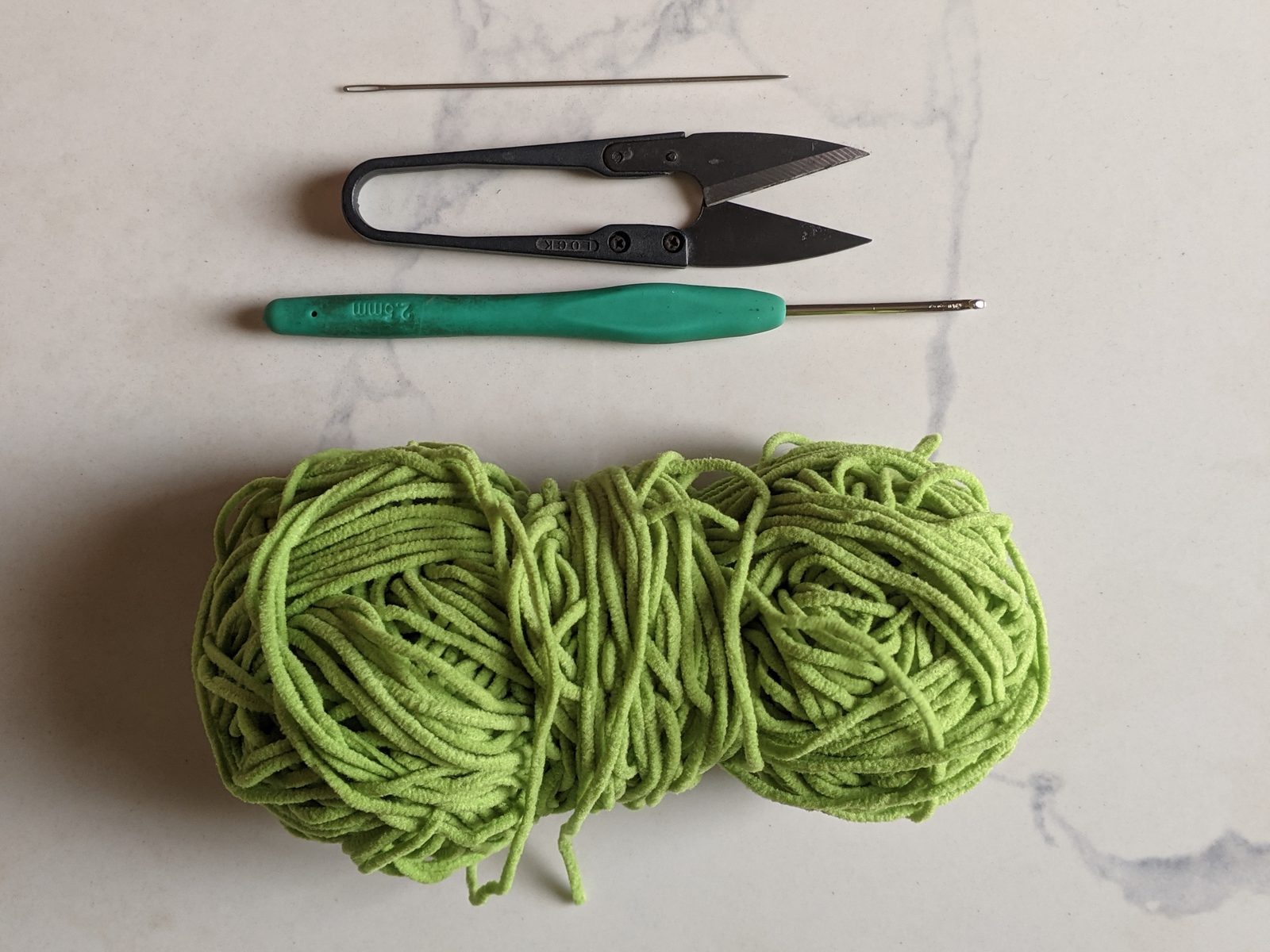 Crochet supplies for the sprout bookmark: a ball of lime green plush yarn, a teal handled crochet hook, a yarn needle and small snips