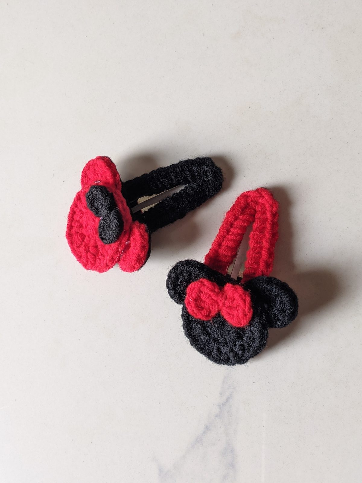 The two colorways of the crochet mouse ears hair clip side by side: red head with black bow and black head with red bow