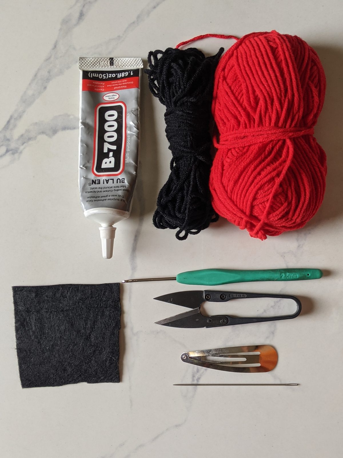 Materials for the crochet mouse ears hair clip: B-7000 glue, black and red milk cotton yarn, black felt, a crochet hook, thread snips, a yarn needle and a metal snap clip