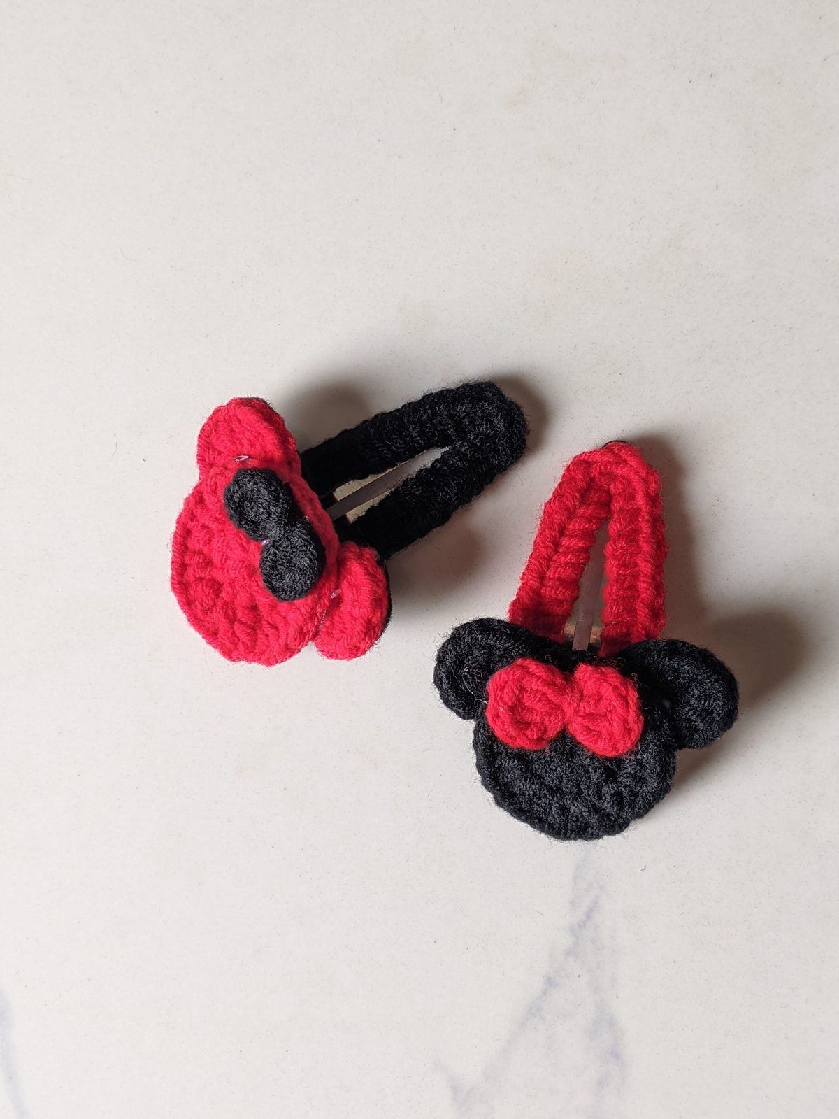 Red crochet mouse ears clip on a black-covered snap clip next to a black mouse ears clip on a red-covered snap clip