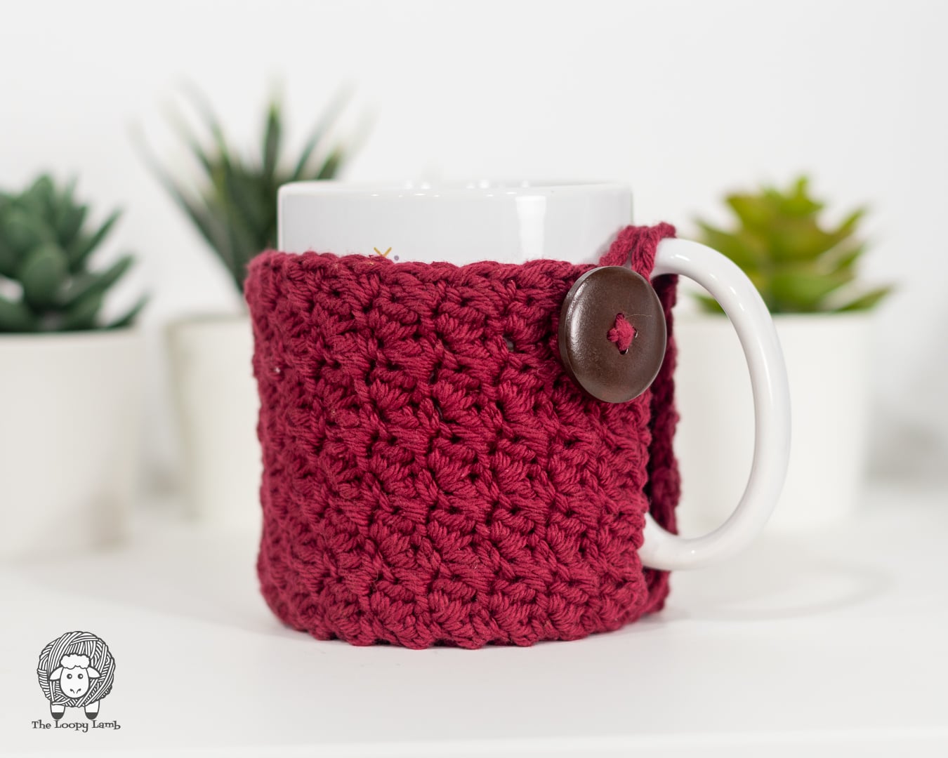 A ribbed crochet mug cozy wrapped around a white mug with a built-in crocheted coaster base, designed by The Loopy Lamb