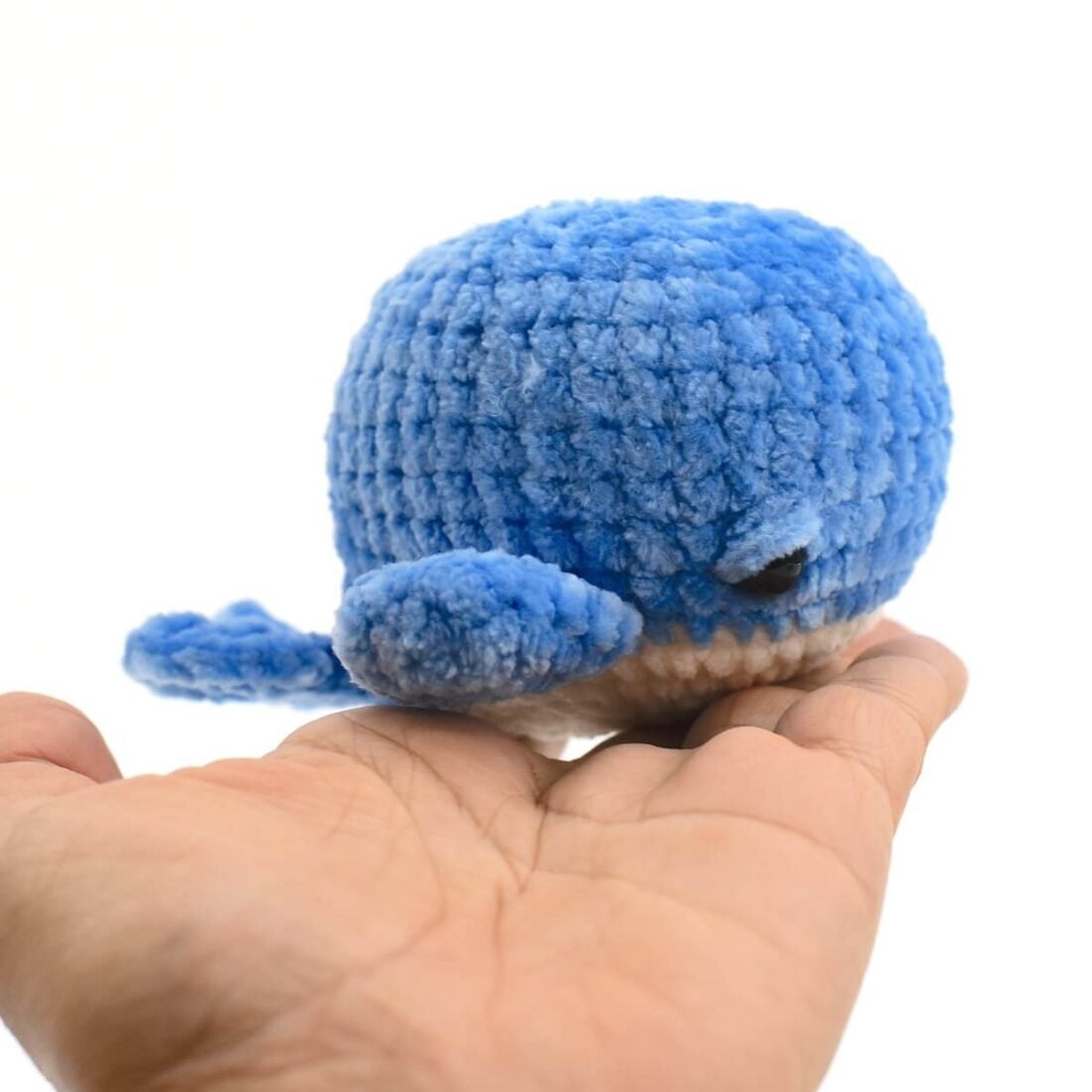 Small blue chenille crochet whale with a cream belly resting on an open palm